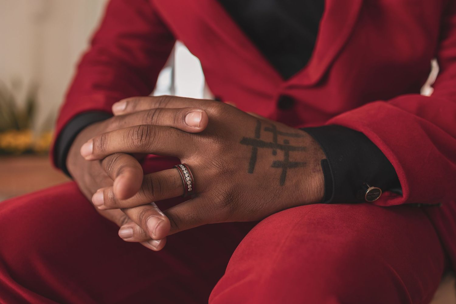 Clasped hands with a wedding ring wearing a red sweater rest on dark pants in meditation or prayer position.