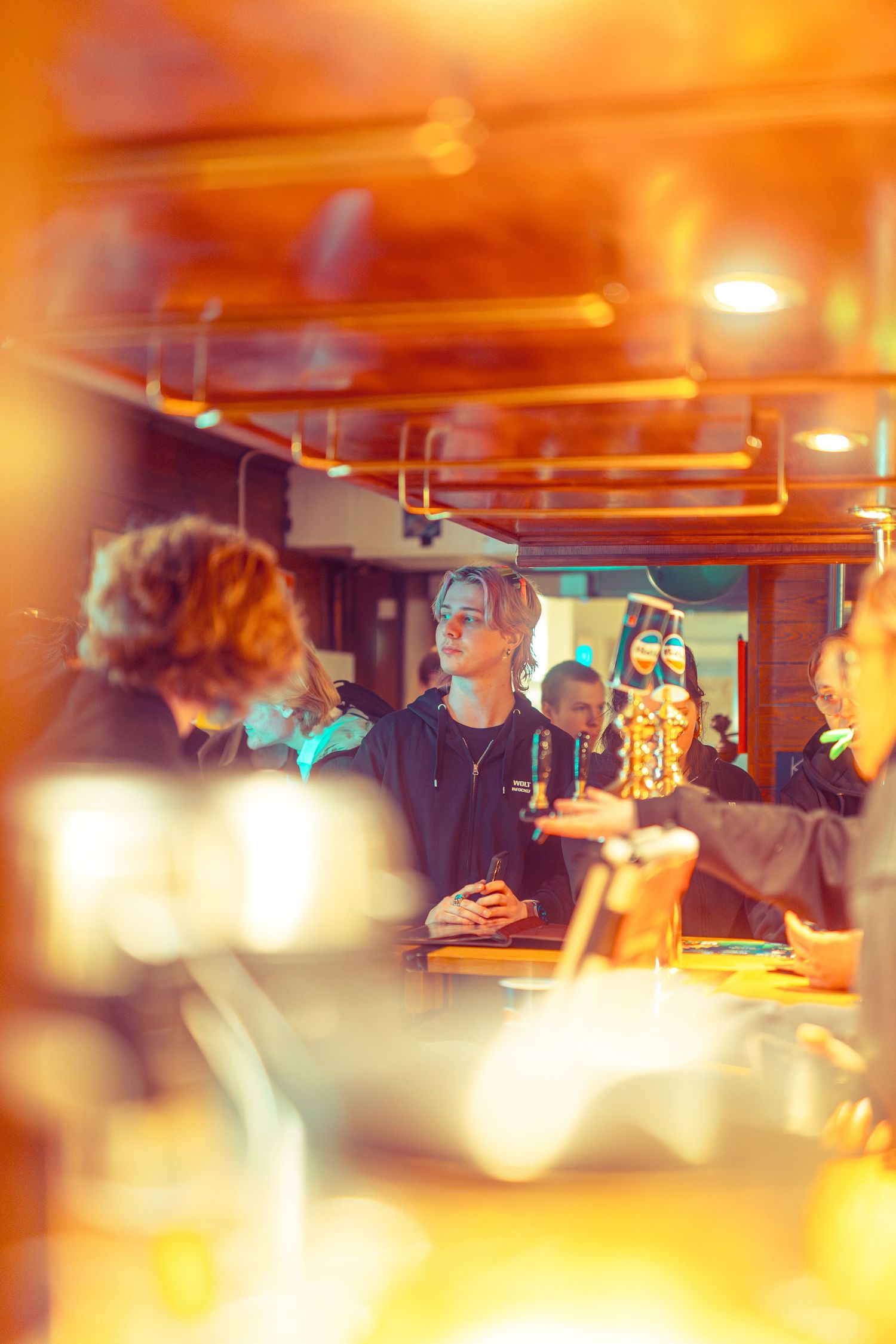 People socializing at a warmly lit bar seen through a bokeh foreground.