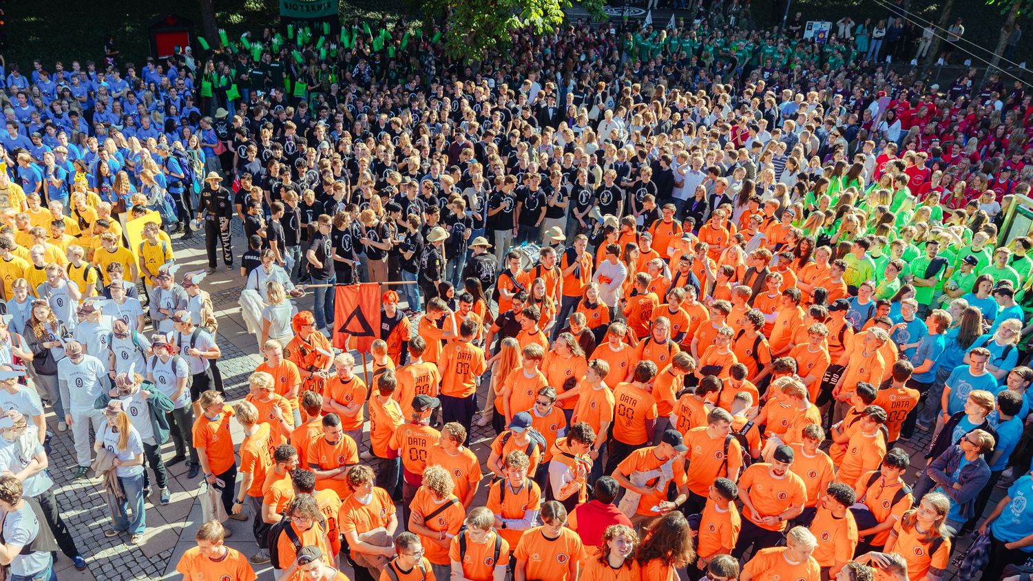 Large crowd of people wearing colorful t-shirts arranged in a rainbow pattern at an outdoor event.