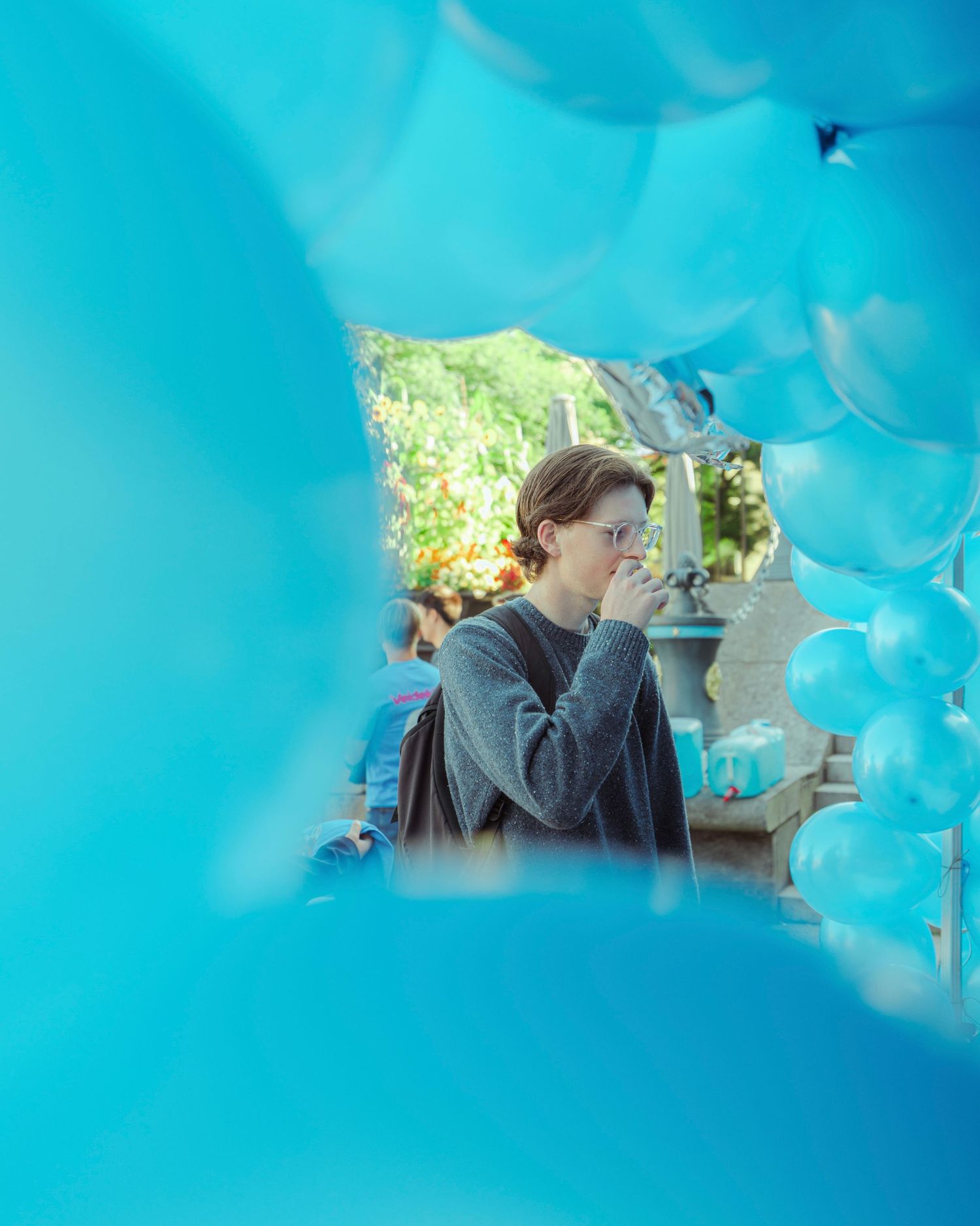 Person surrounded by vibrant turquoise balloons at an outdoor event, viewed through a gap in the balloon display.