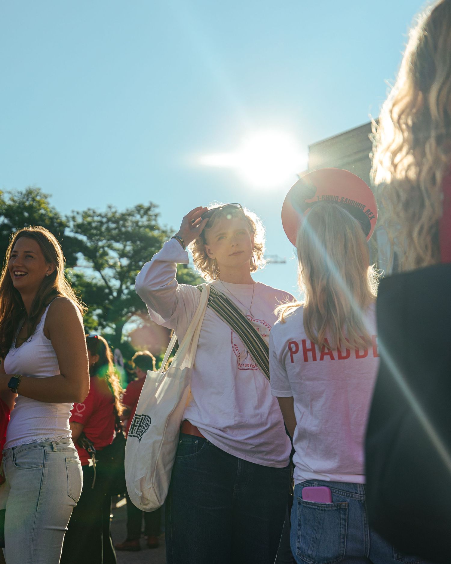 Young women in pink sorority shirts gather outdoors on a sunny day, smiling and socializing at a campus event.