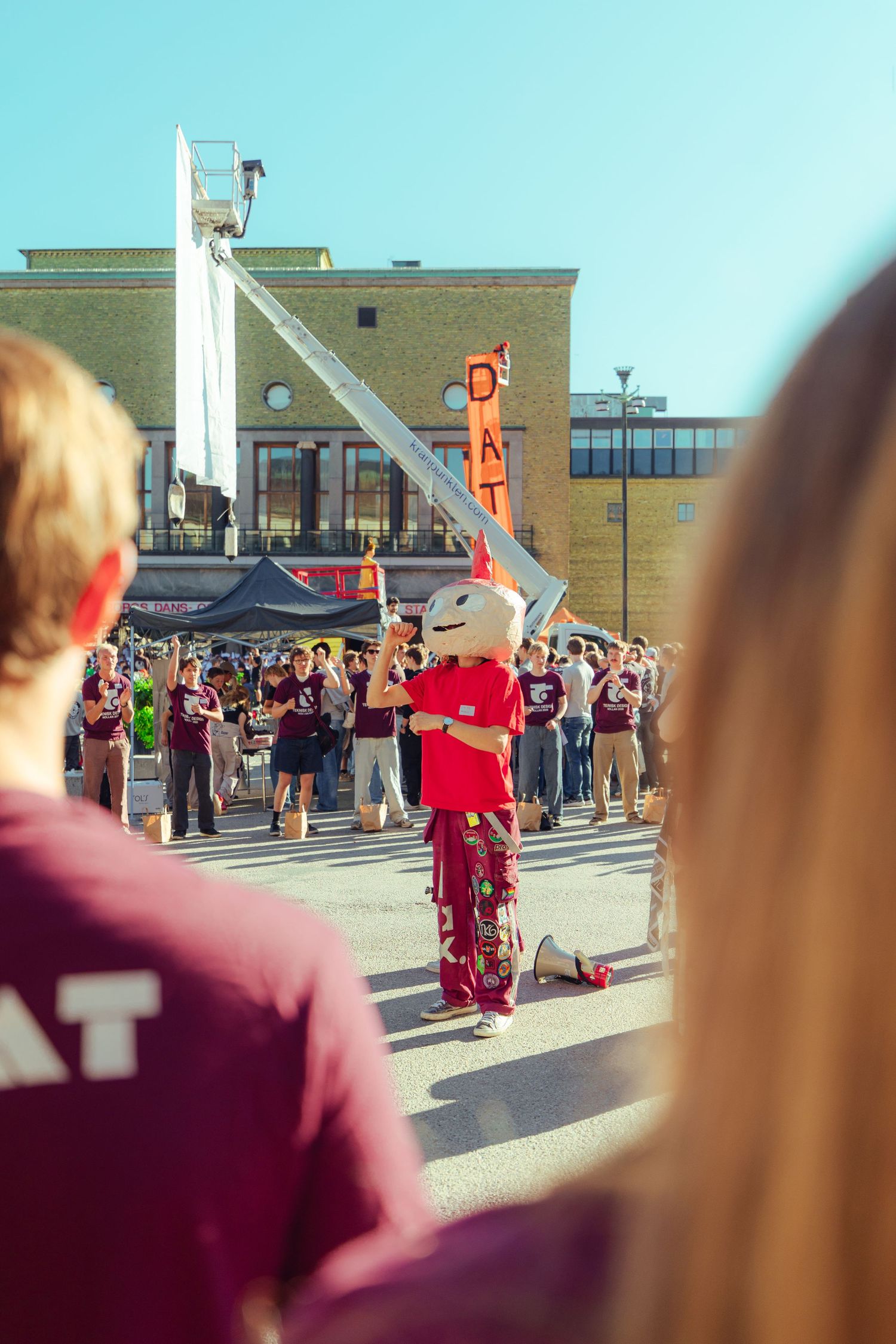 A mascot in red costume performs outdoors at a crowded Texas A&M event on a sunny day.