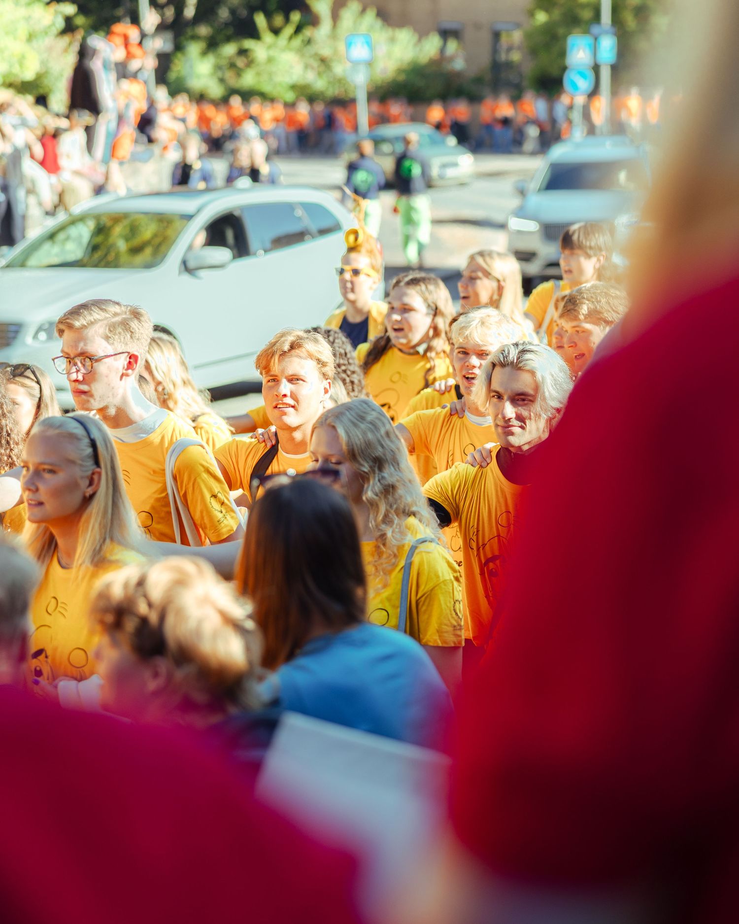 Large group of young people wearing matching yellow t-shirts marching together outdoors during a sunny day event.