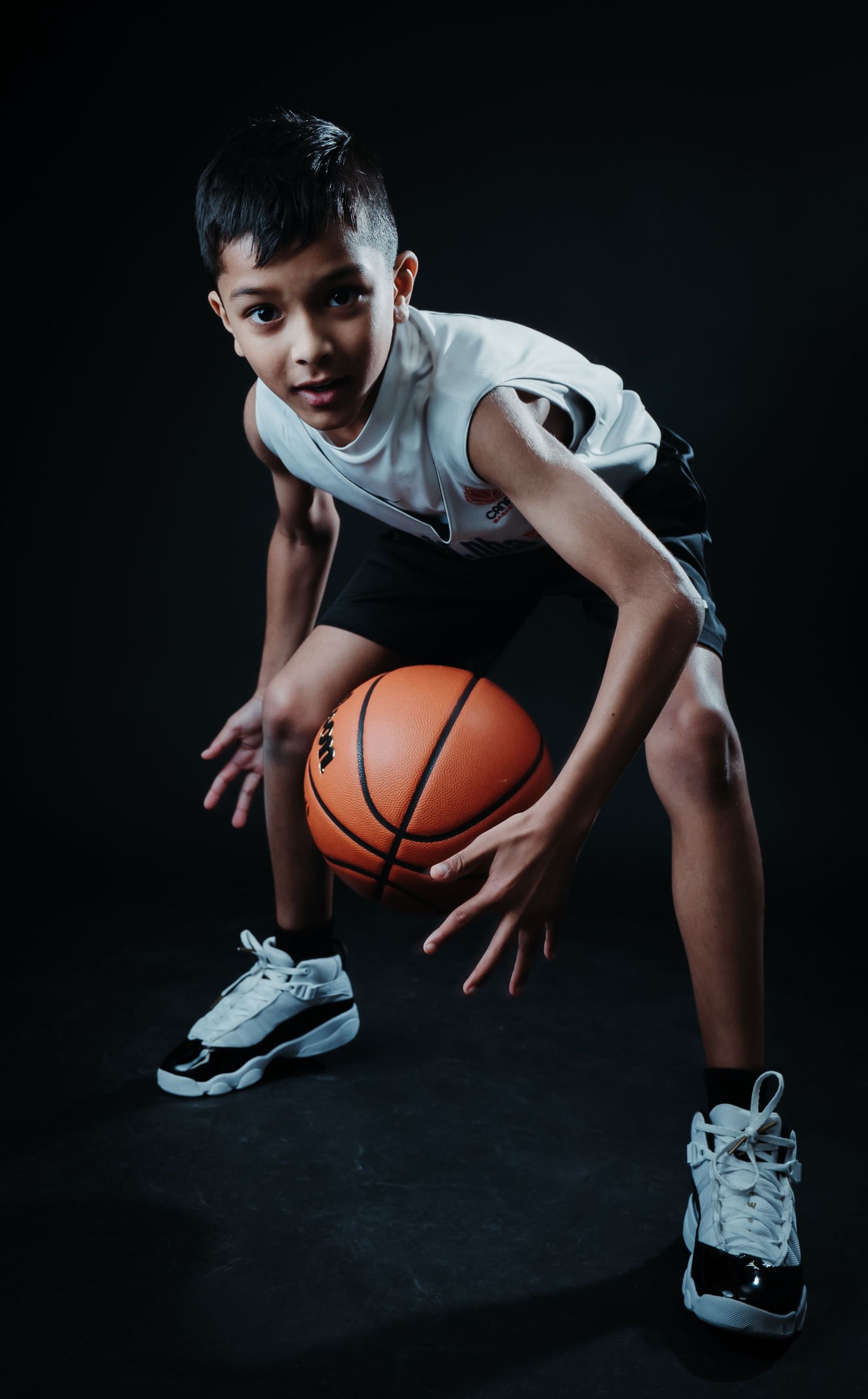 Basketball player posing confidently in a studio portrait, wearing a basketball uniform and holding a basketball, with dramatic lighting