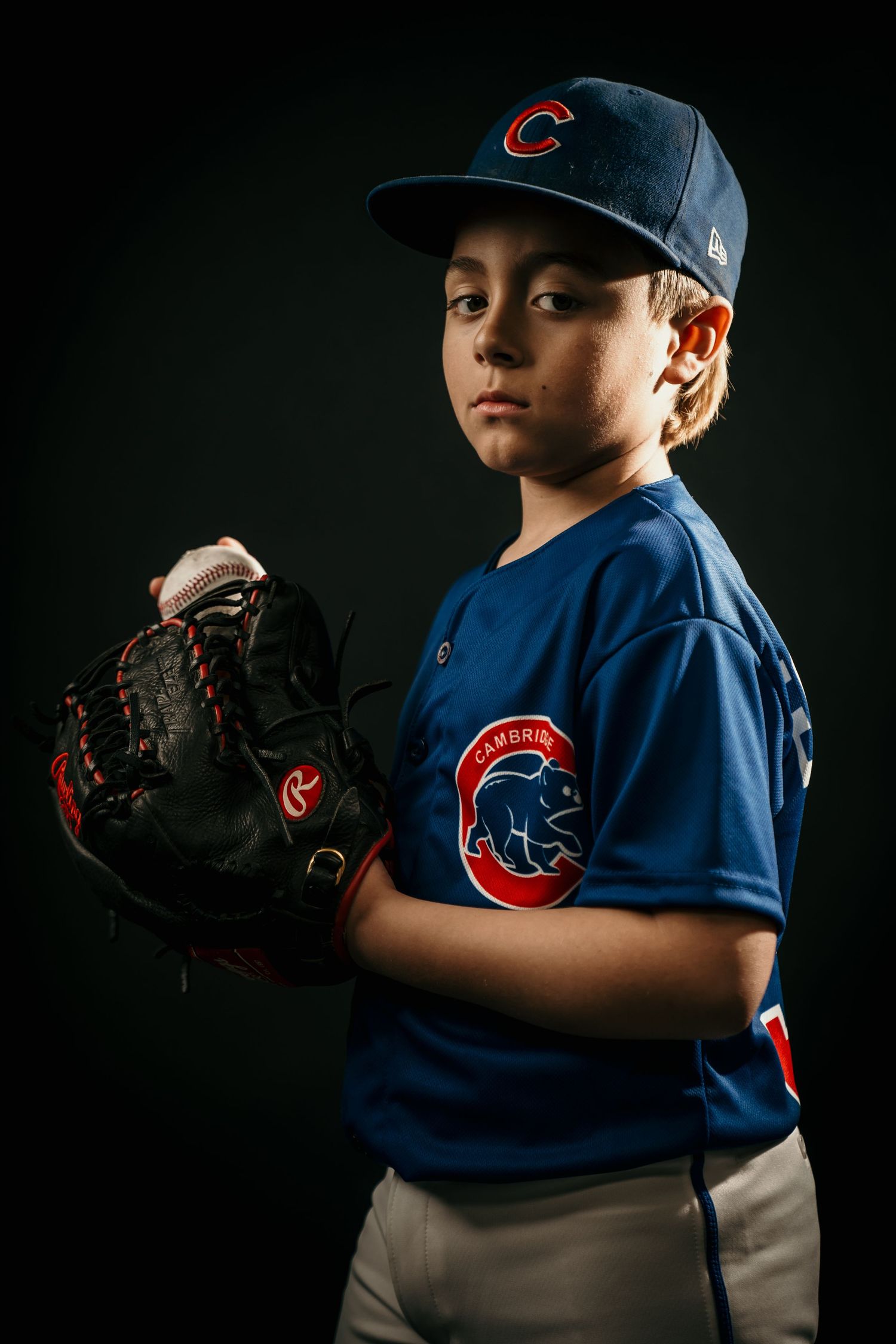 Young baseball player posing confidently in a studio portrait, wearing a baseball uniform and holding a baseball bat, with dramatic lighting