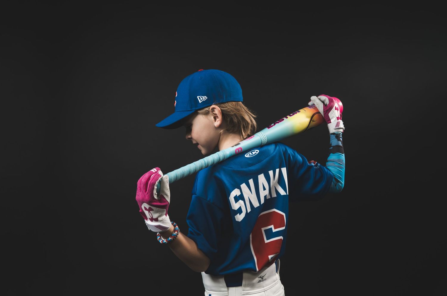 Young baseball player posing confidently in a studio portrait, wearing a baseball uniform and holding a baseball bat, with dramatic lighting