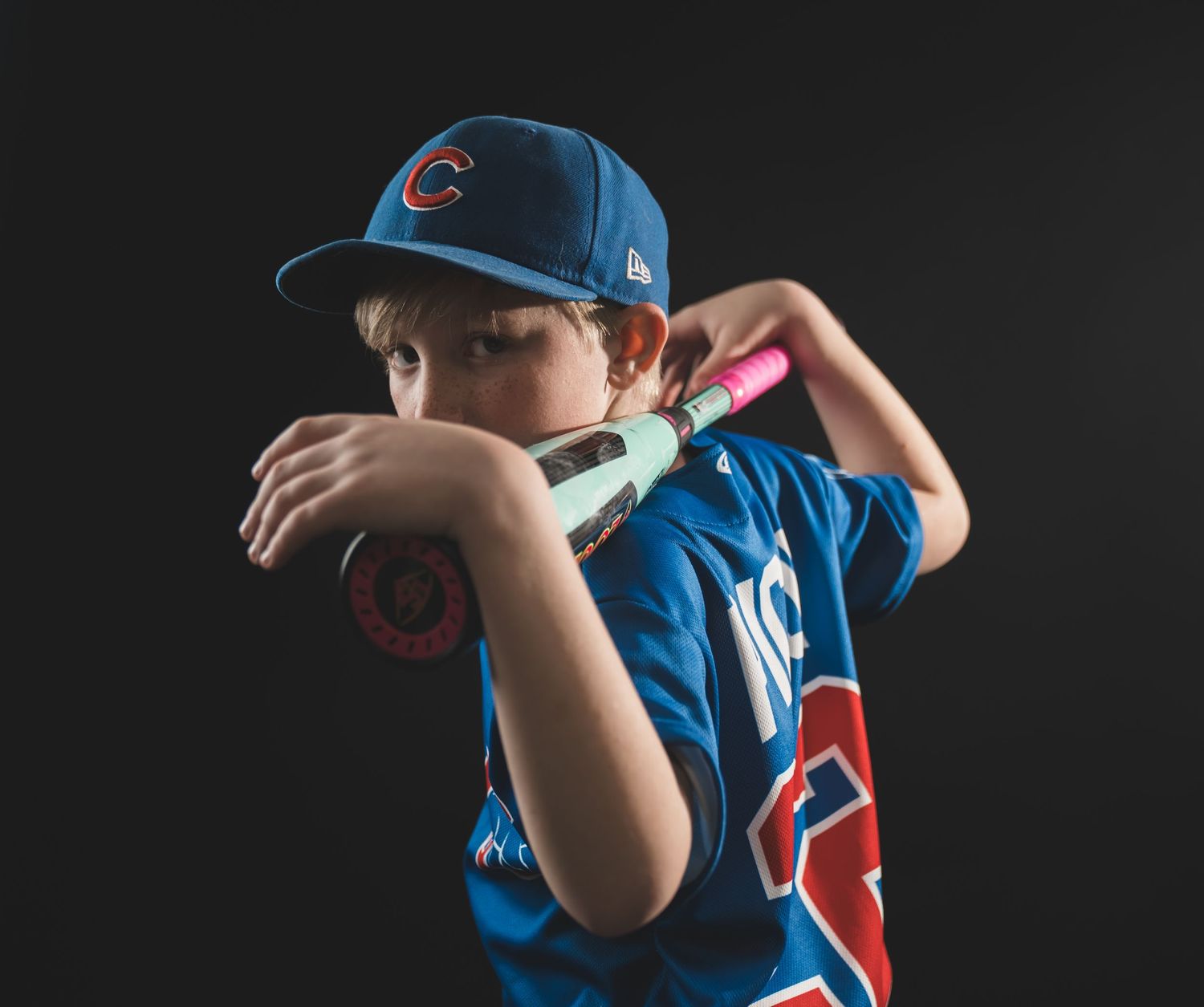 Young baseball player posing confidently in a studio portrait, wearing a baseball uniform and holding a baseball bat, with dramatic lighting