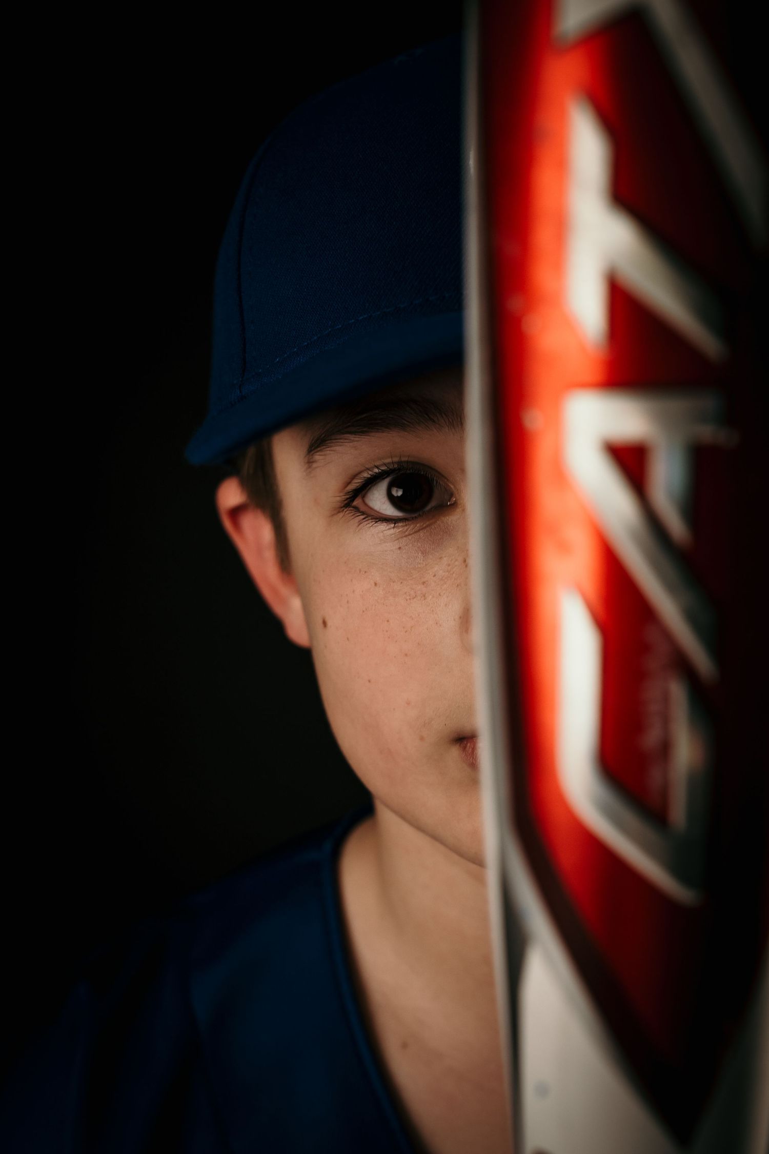Young baseball player posing confidently in a studio portrait, wearing a baseball uniform and holding a baseball bat, with dramatic lighting