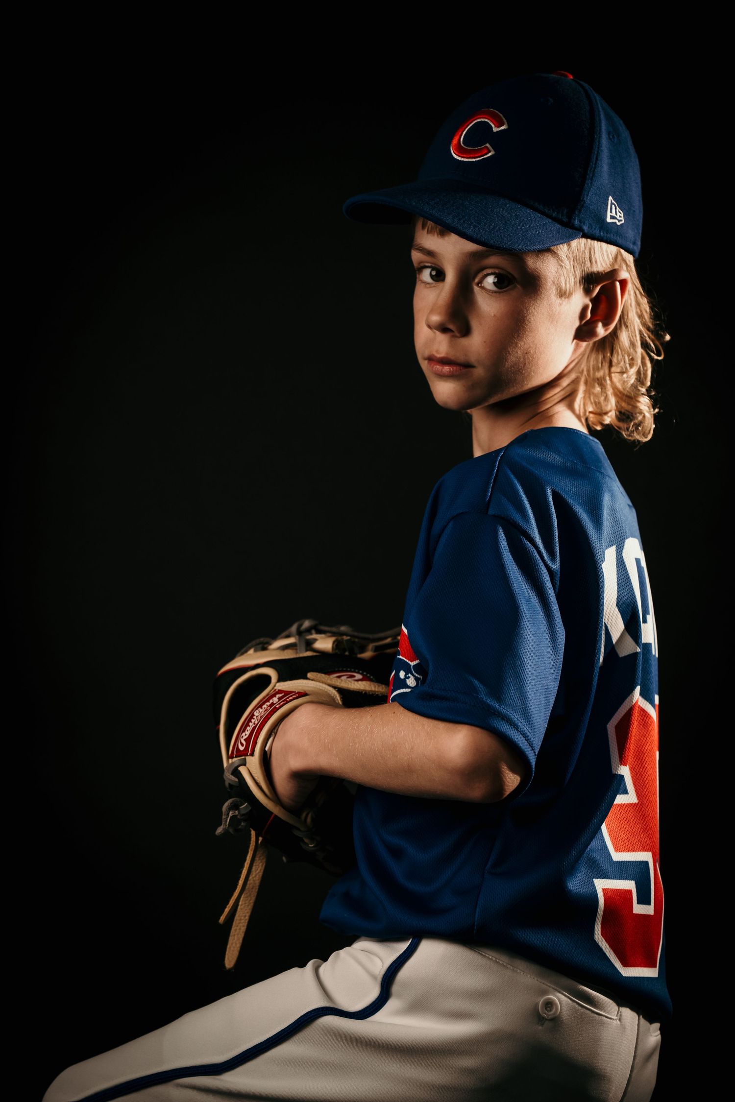 Young baseball player posing confidently in a studio portrait, wearing a baseball uniform and holding a baseball bat, with dramatic lighting