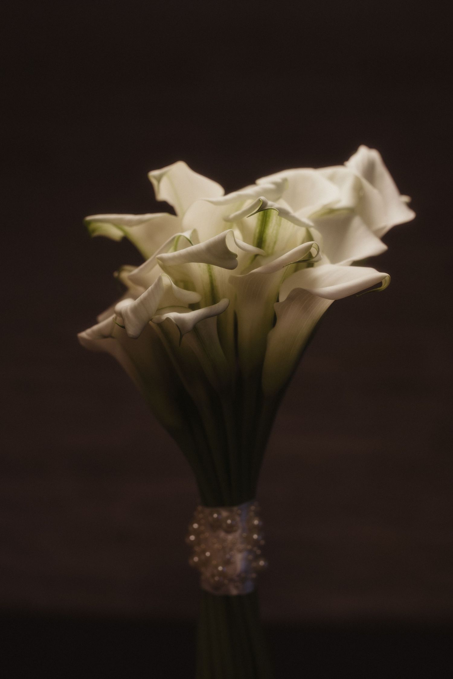 Beautiful white calla lily wedding bouquet tied with pearl bracelet against dark background.
