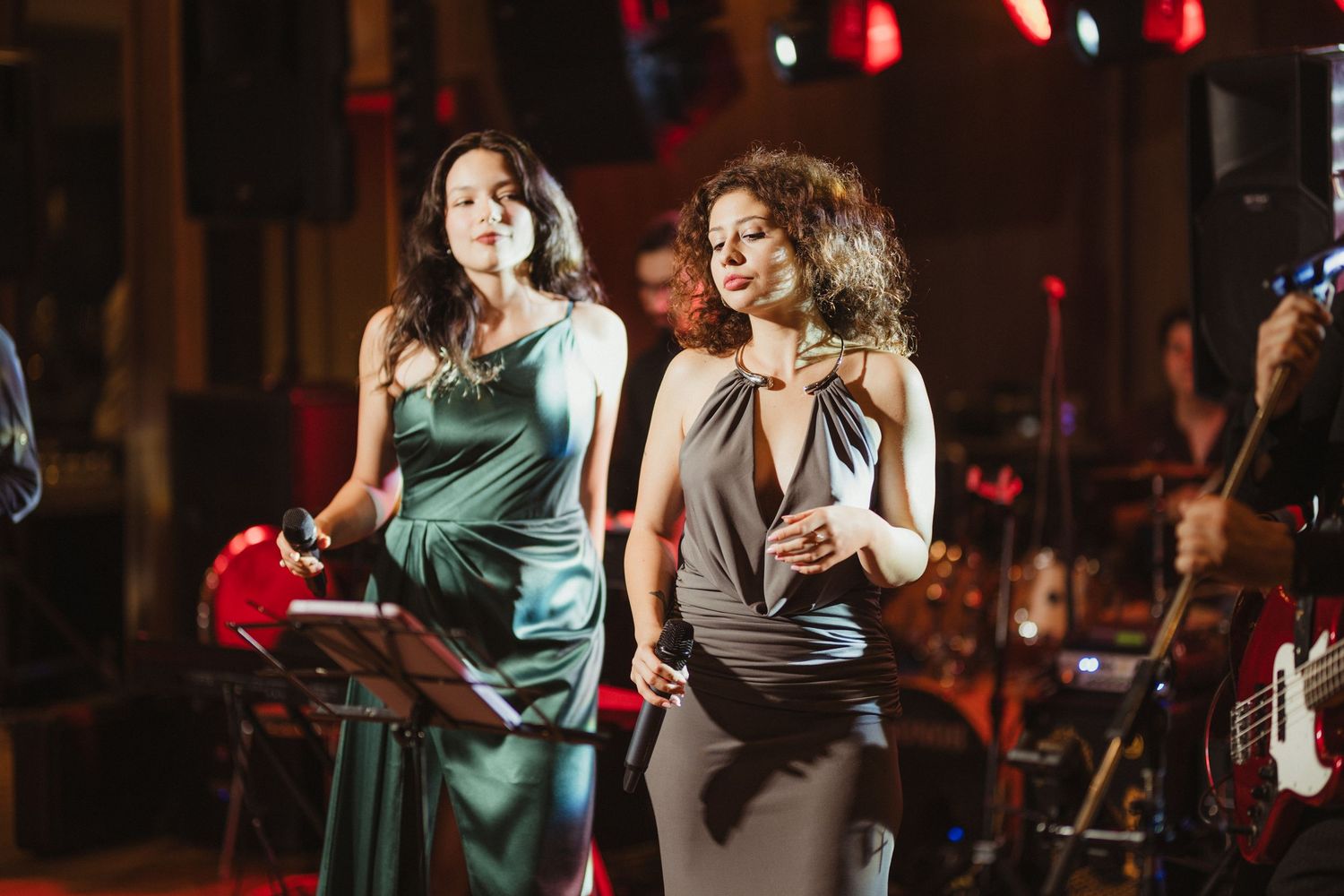 Two female singers in elegant gowns performing on stage at a live music event.