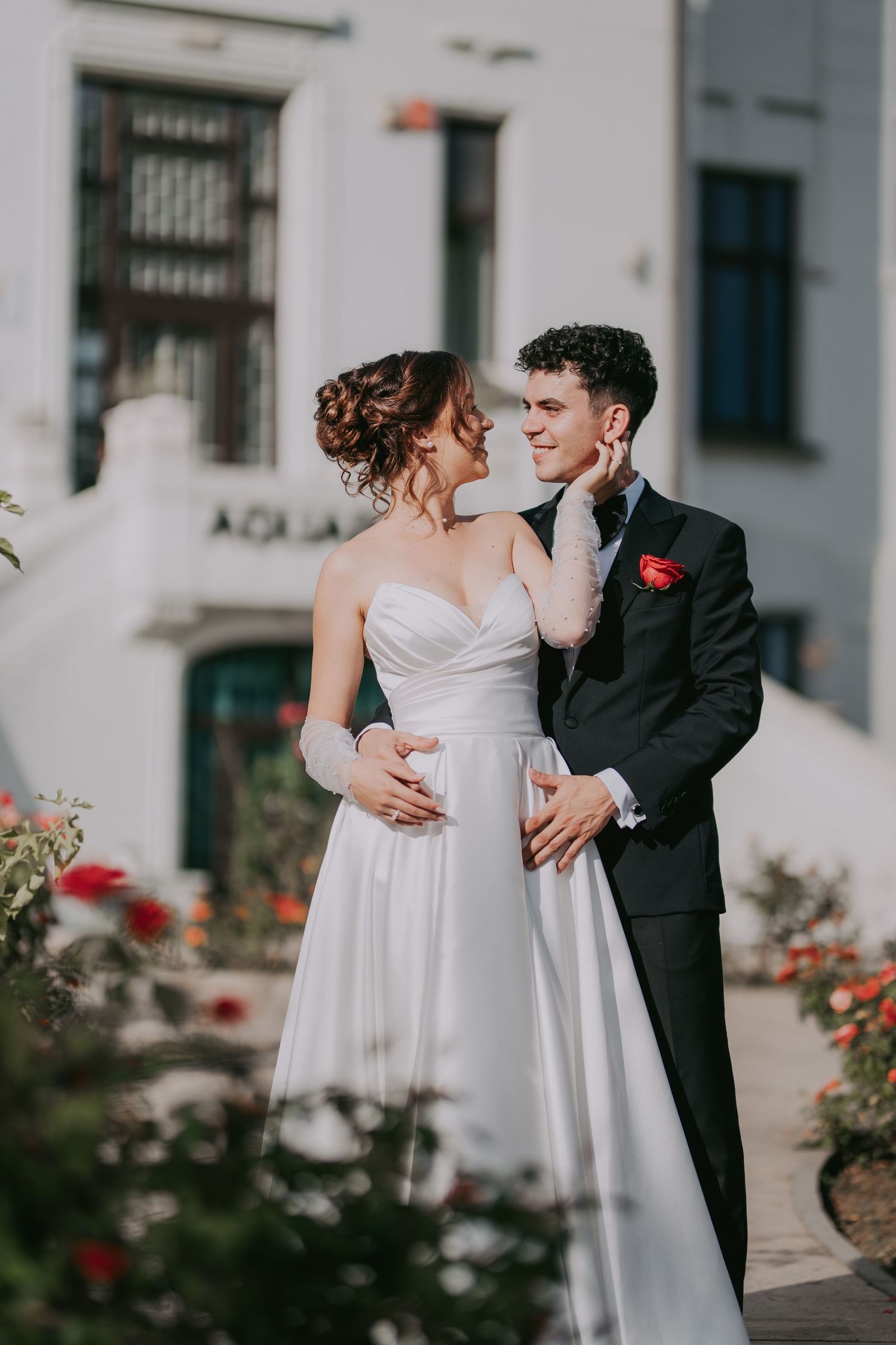 Bride and groom sharing a romantic moment in front of a white building with red roses. Epicu Fotograf Drobeta-Turnu Severin