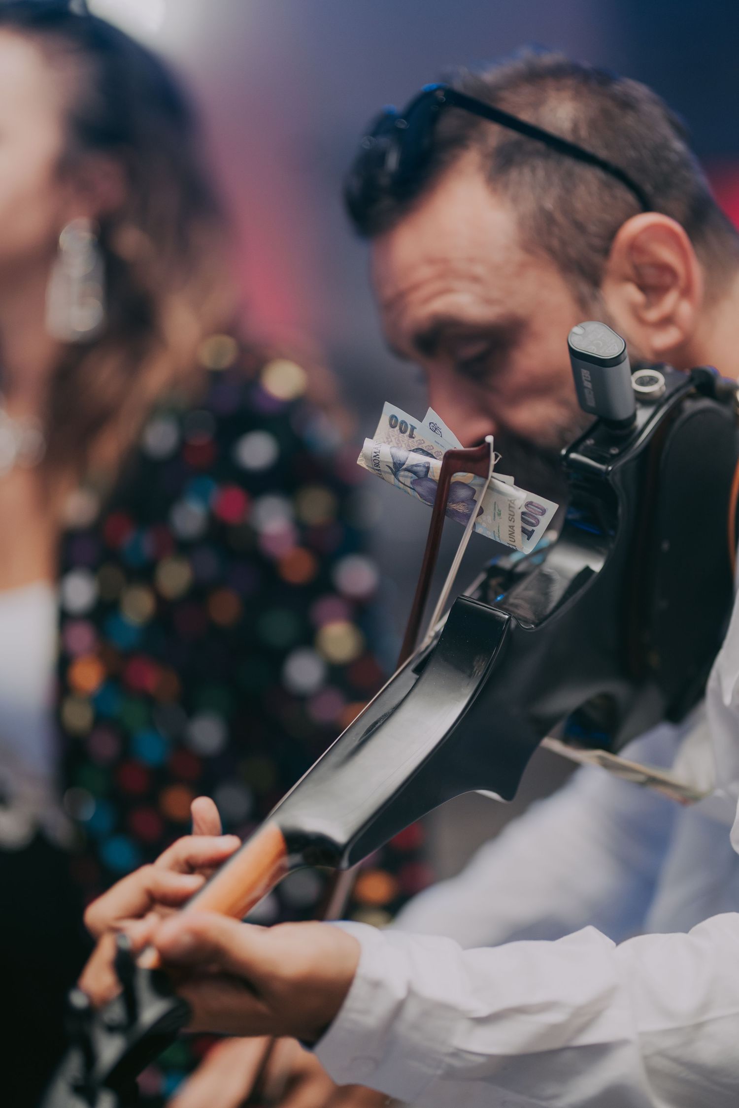 Musician plays a black electric violin with banknotes tucked in at a vibrant wedding reception. Epicu Fotograf Drobeta-Turnu Severin