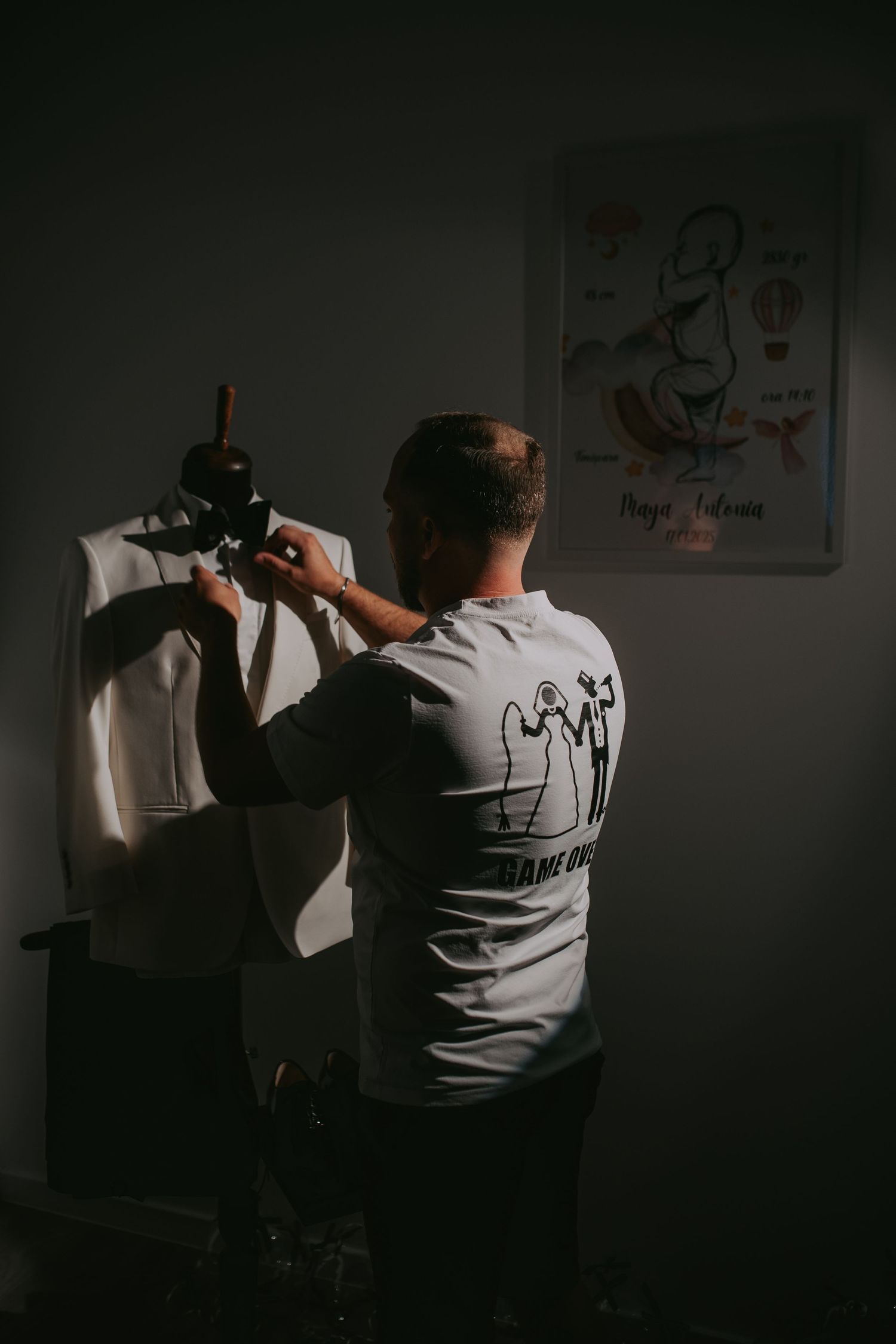 Man adjusting a white suit jacket on a tailor's mannequin in a dimly lit room. Epicu Fotograf Drobeta-Turnu Severin