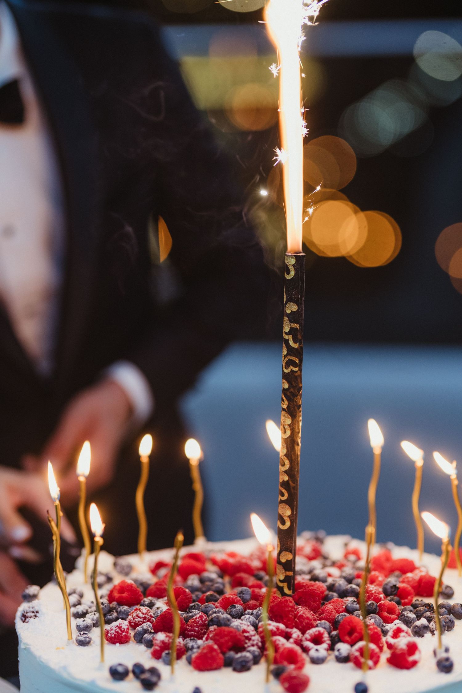Close-up of a white wedding cake topped with fresh raspberries, blueberries, and lit candles with a sparkler. Epicu Fotograf Drobeta-Turnu S