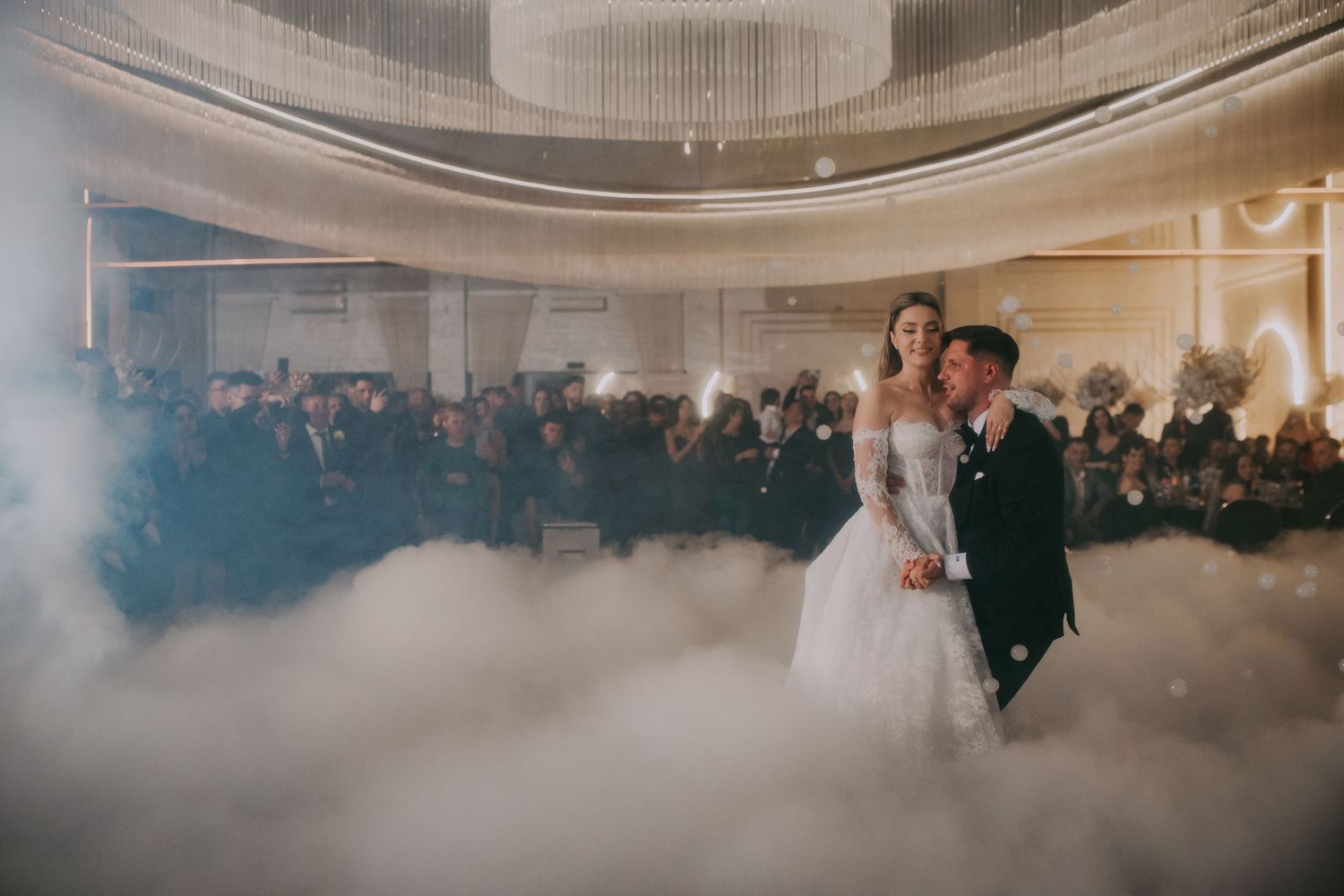 Bride and groom share first dance surrounded by dramatic fog effects on elegant wedding reception floor.