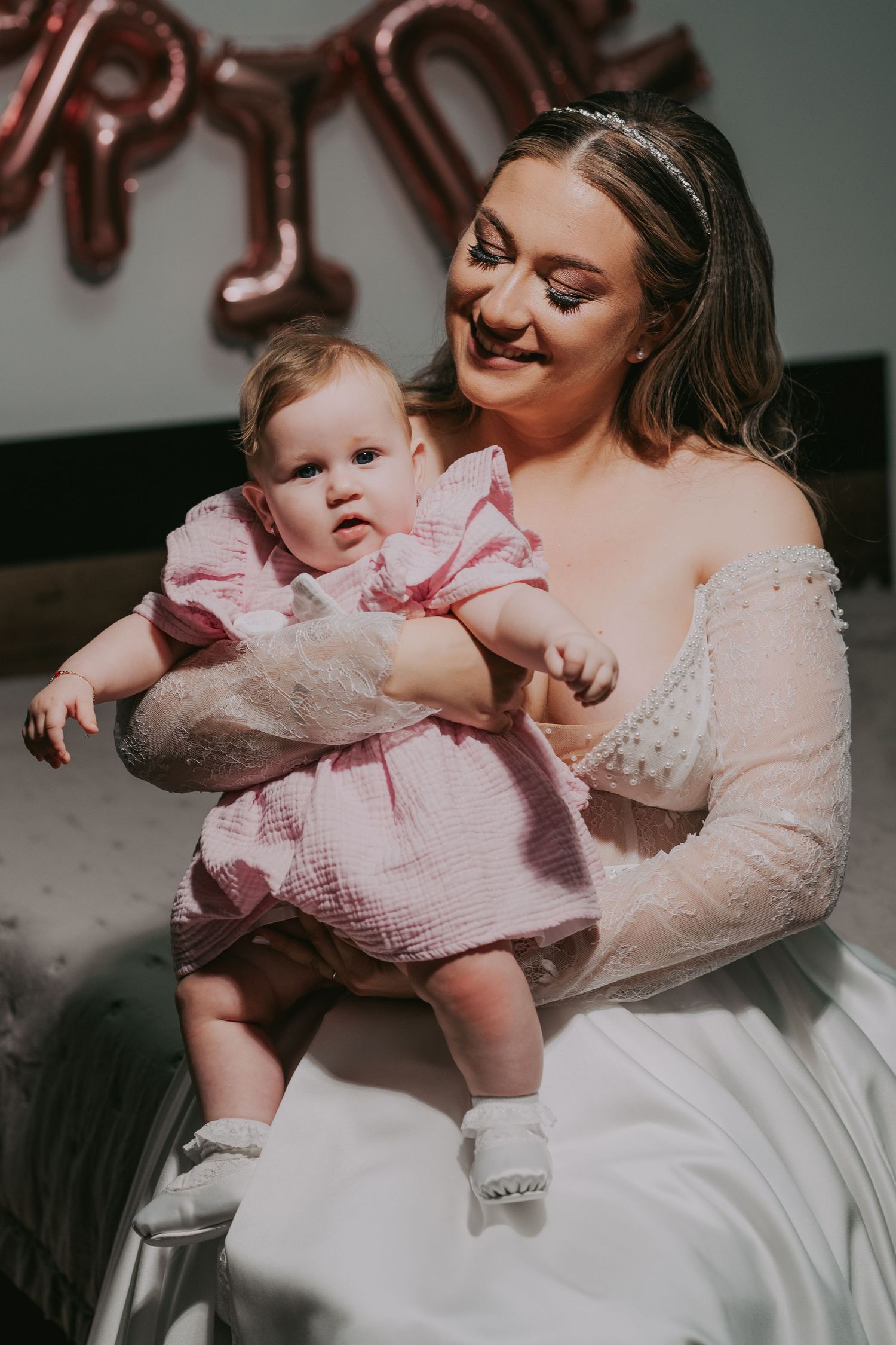 Bride in a lace wedding gown lovingly holding a baby girl in a pink dress at her wedding. Epicu Fotograf Drobeta-Turnu Severin