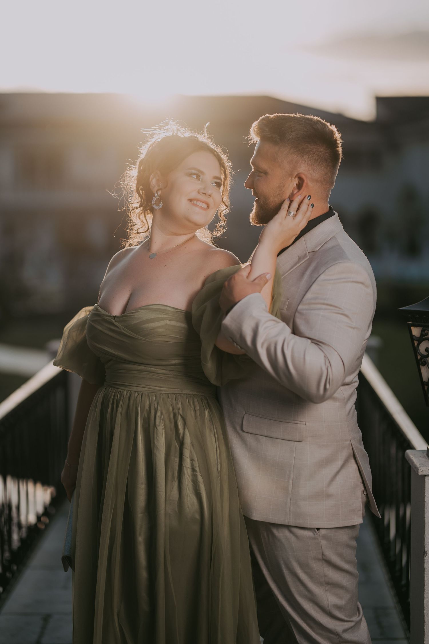 Couple in elegant attire embracing at sunset on a bridge, woman in green gown and man in gray suit. Epicu Fotograf Drobeta-Turnu Severin