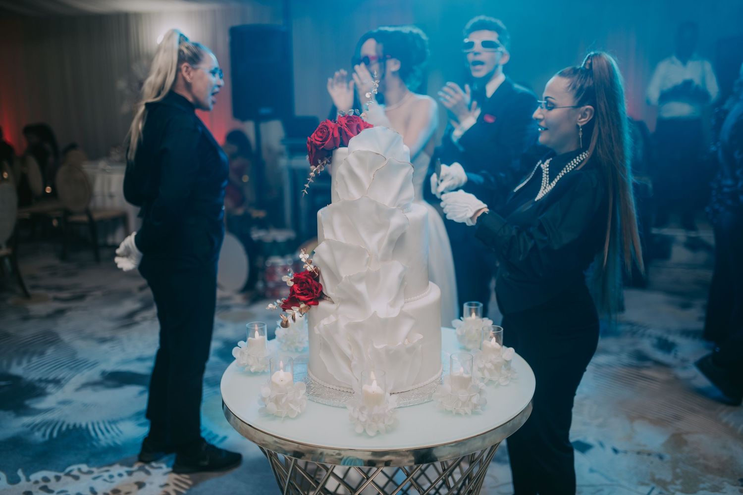 Bride and groom cutting elegant white tiered wedding cake surrounded by guests at a formal reception. Epicu Fotograf Drobeta-Turnu Severin