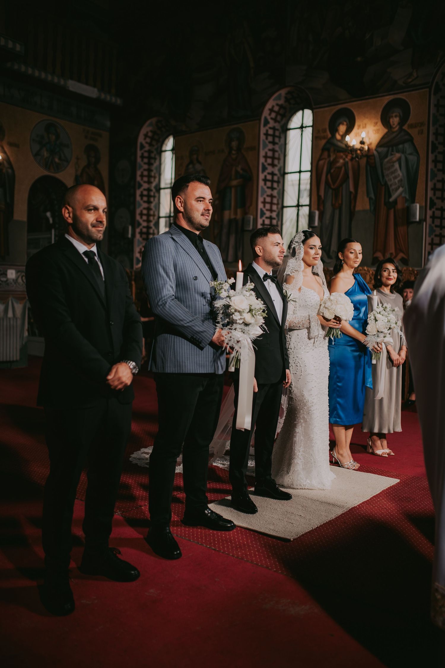 Wedding party stands at Orthodox church altar with icons and candles during ceremony.
