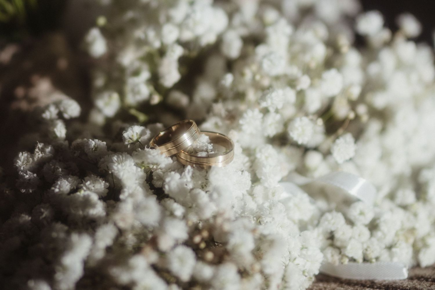 Two gold wedding rings resting on delicate white baby breath flowers with soft bokeh background.