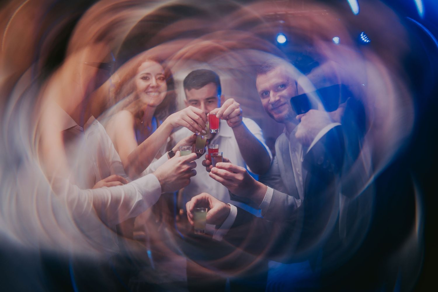 Wedding guests toasting with red drinks captured in a dreamy swirling long-exposure photograph. Epicu Fotograf Drobeta-Turnu Severin