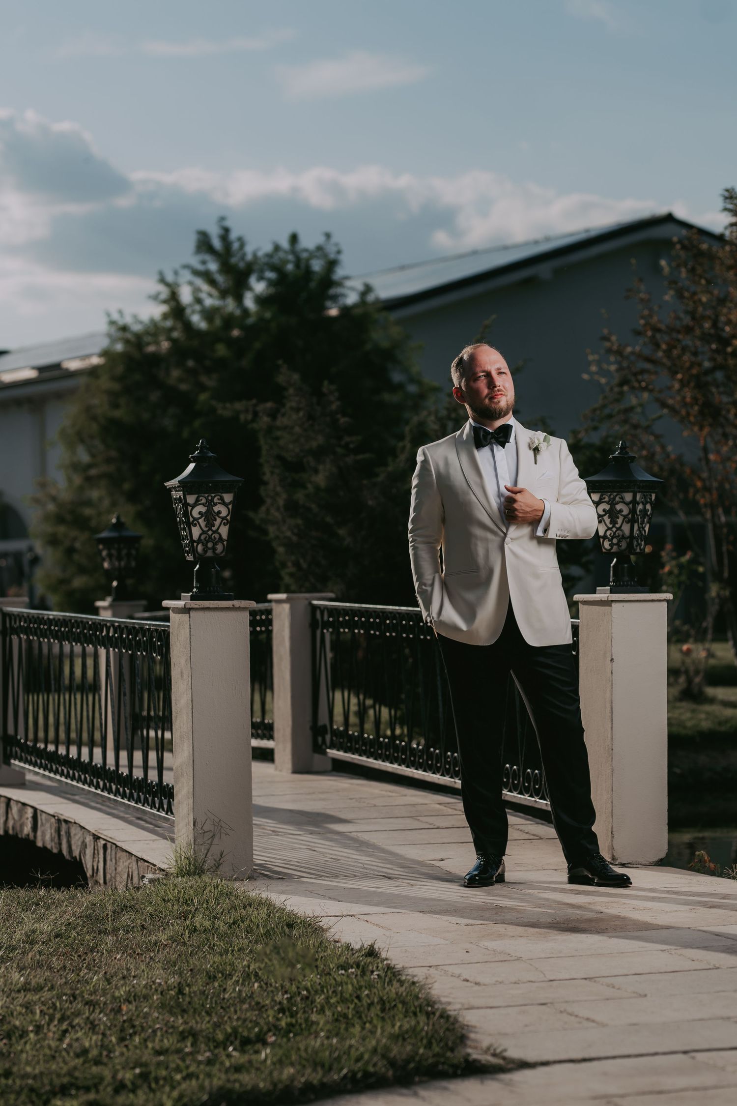 Dapper groom in white tuxedo jacket and black bow tie poses confidently on outdoor pathway. Epicu Fotograf Drobeta-Turnu Severin