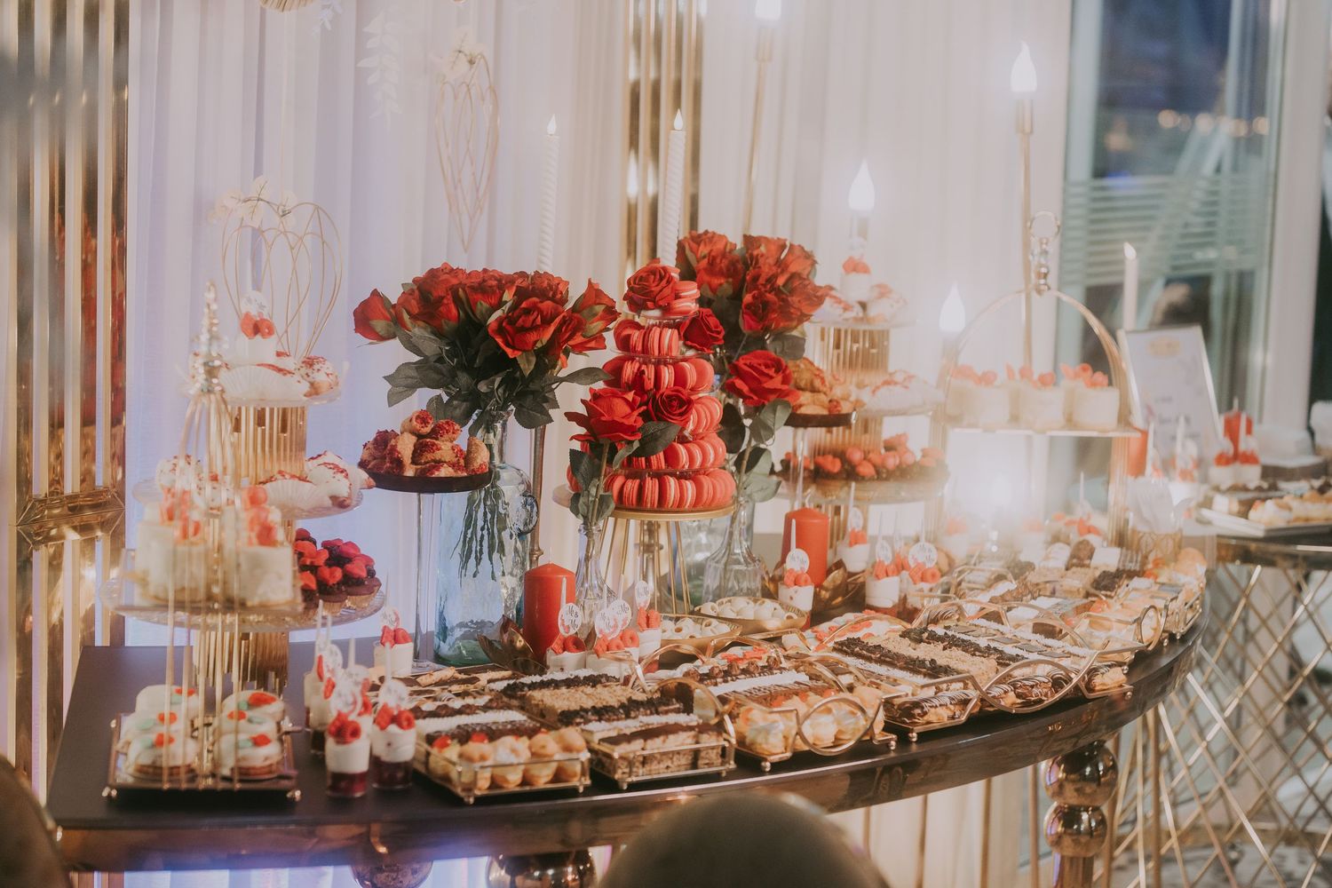 Wedding dessert table with red roses, macaron tower, pastries, and warm string light backdrop. Epicu Fotograf Drobeta-Turnu Severin