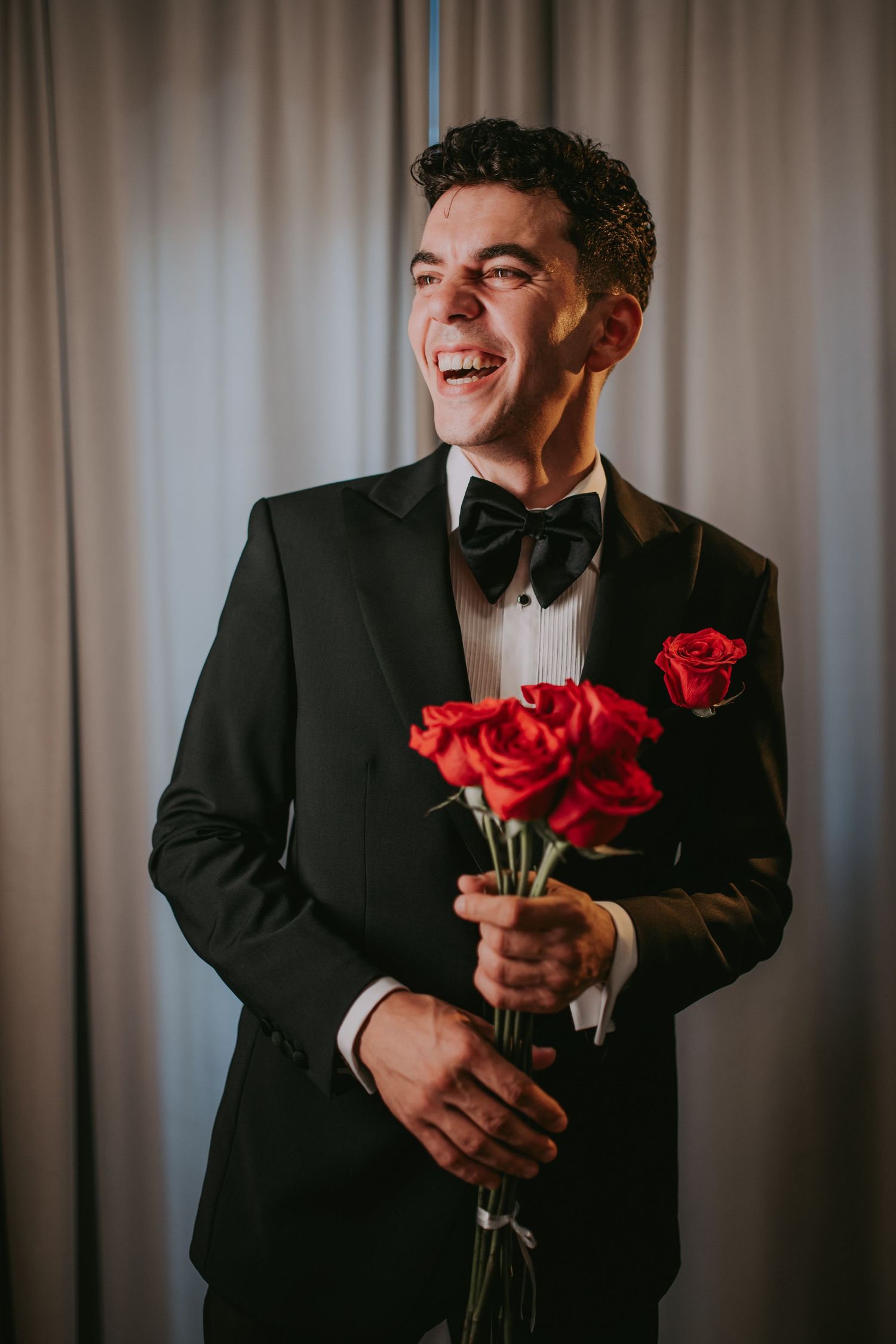 Joyful groom in black tuxedo with bow tie holding red roses and laughing. Epicu Fotograf Drobeta-Turnu Severin