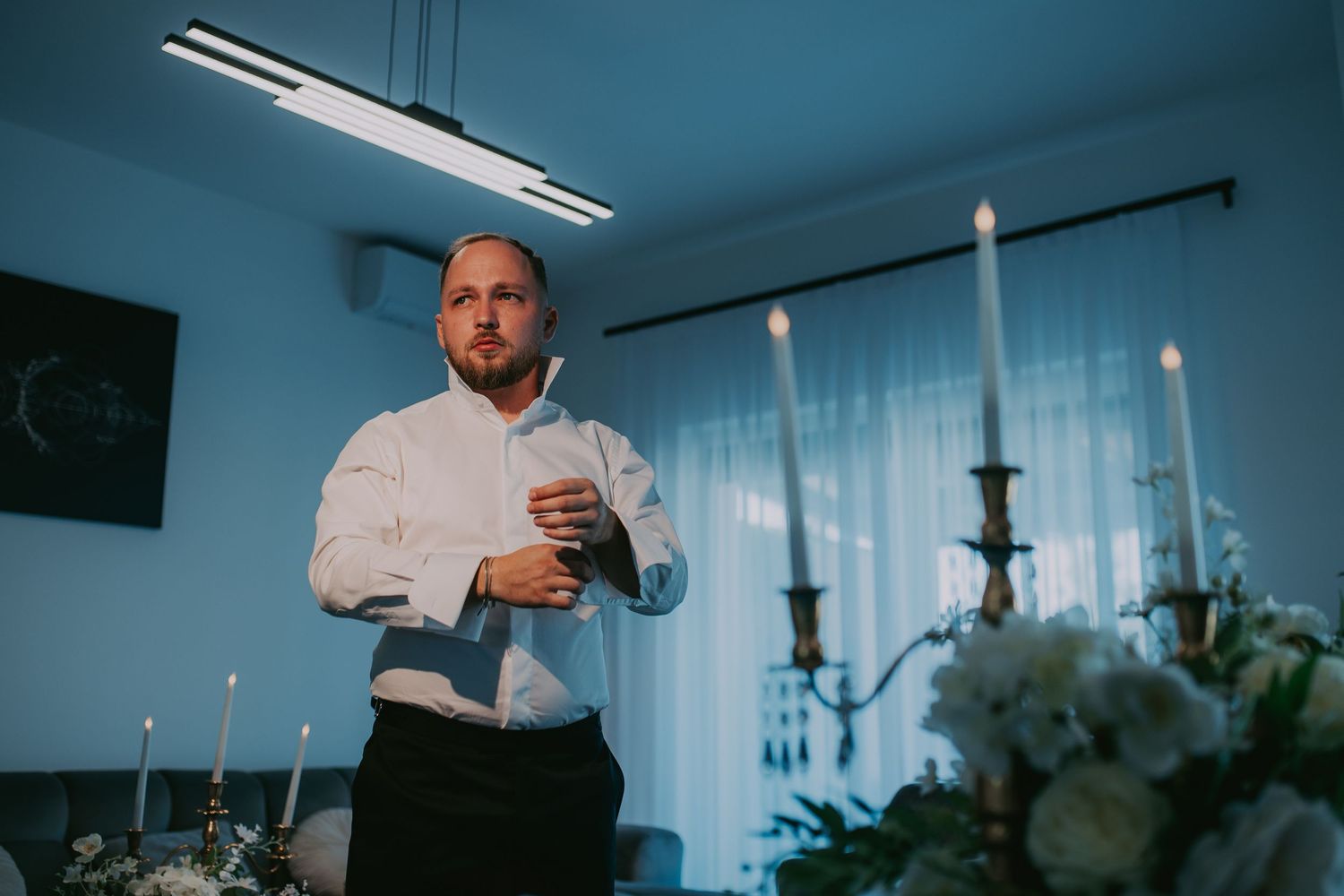 Elegant groom in white shirt adjusting cufflinks in a candlelit room before wedding. Epicu Fotograf Drobeta-Turnu Severin