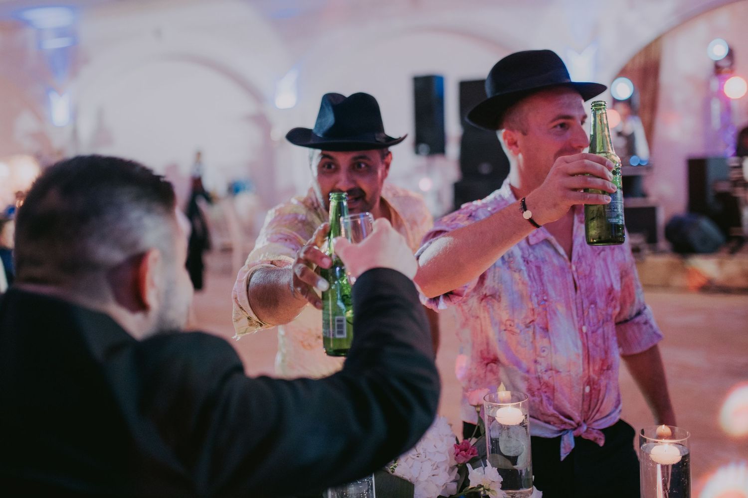 Three men in black hats toasting with beer bottles at a festive wedding reception party. Epicu Fotograf Drobeta-Turnu Severin