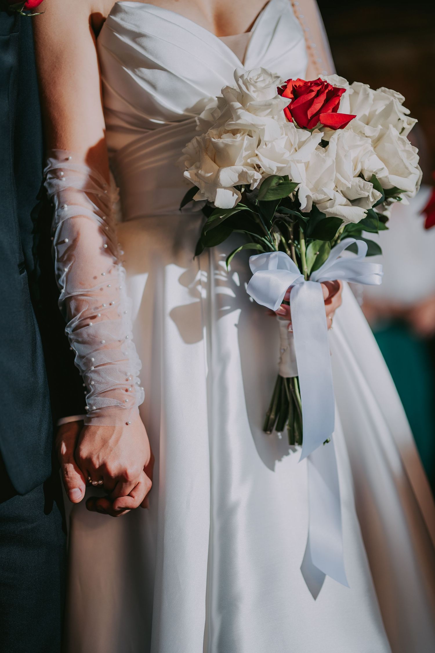 Bride holds white and red rose bouquet tied with ribbon while groom holds her hand. Epicu Fotograf Drobeta-Turnu Severin