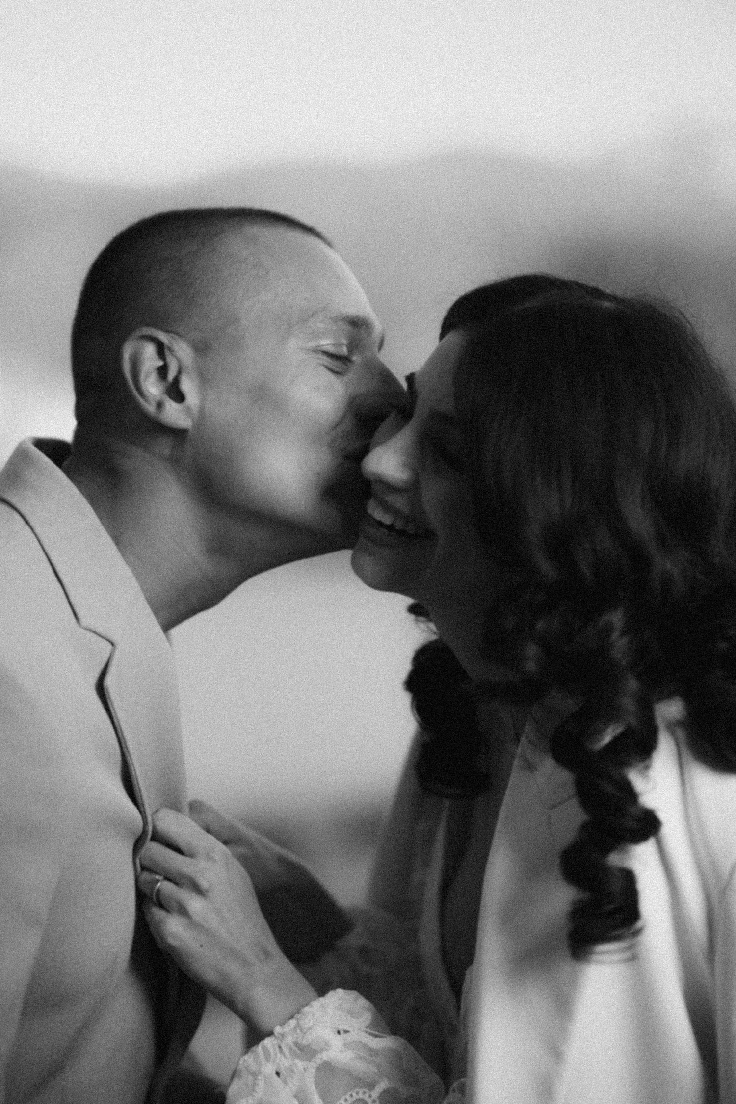 Black and white intimate moment of groom kissing smiling bride on the cheek.
