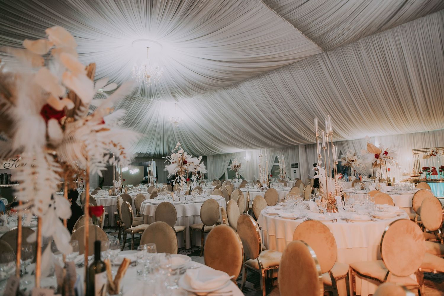 Elegantly decorated wedding reception tent with tall floral centerpieces and round tables. Epicu Fotograf Drobeta-Turnu Severin