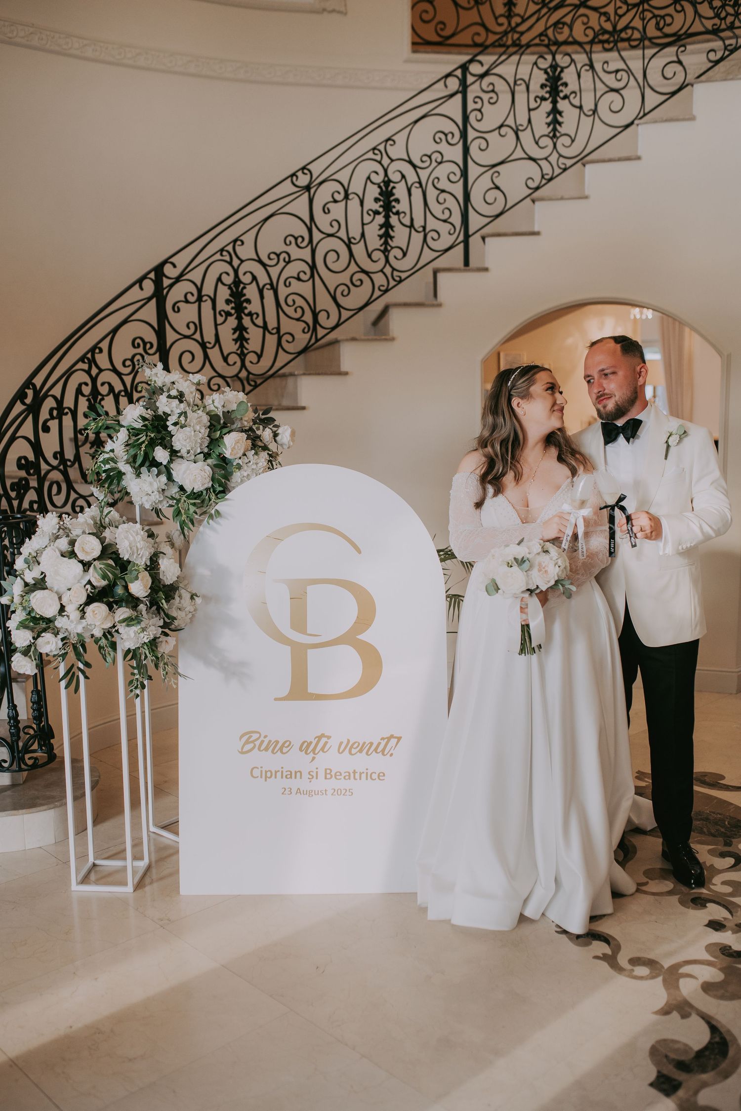 Bride and groom pose beside personalized welcome sign at foot of ornate iron staircase. Epicu Fotograf Drobeta-Turnu Severin