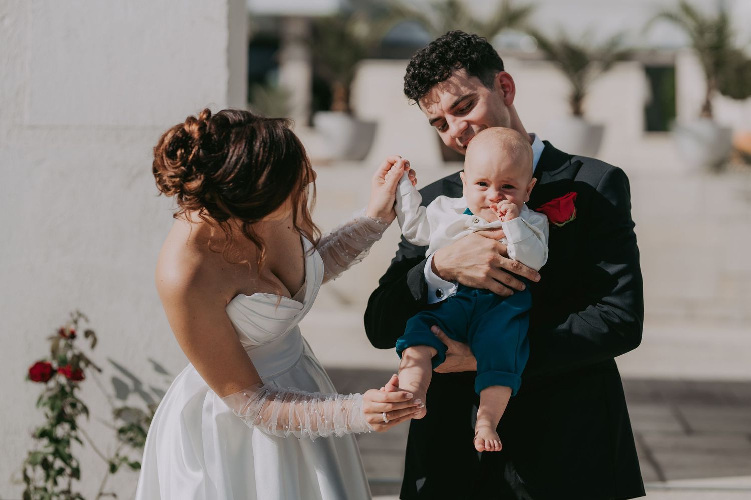 Bride and groom holding a baby boy in a blue suit at an outdoor wedding ceremony. Epicu Fotograf Drobeta-Turnu Severin
