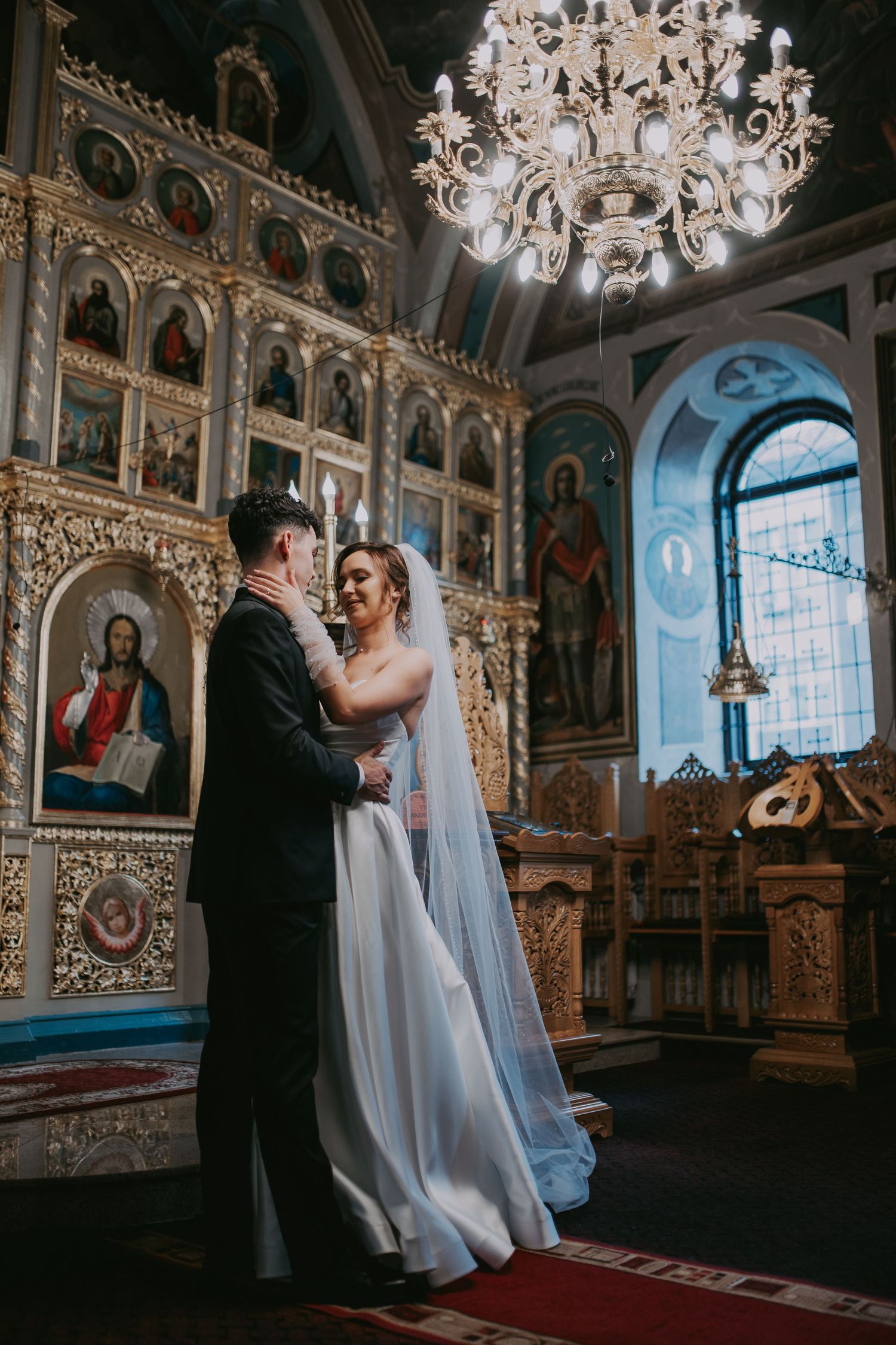 Newlyweds embracing inside beautifully decorated Orthodox church with golden iconostasis. Epicu Fotograf Drobeta-Turnu Severin