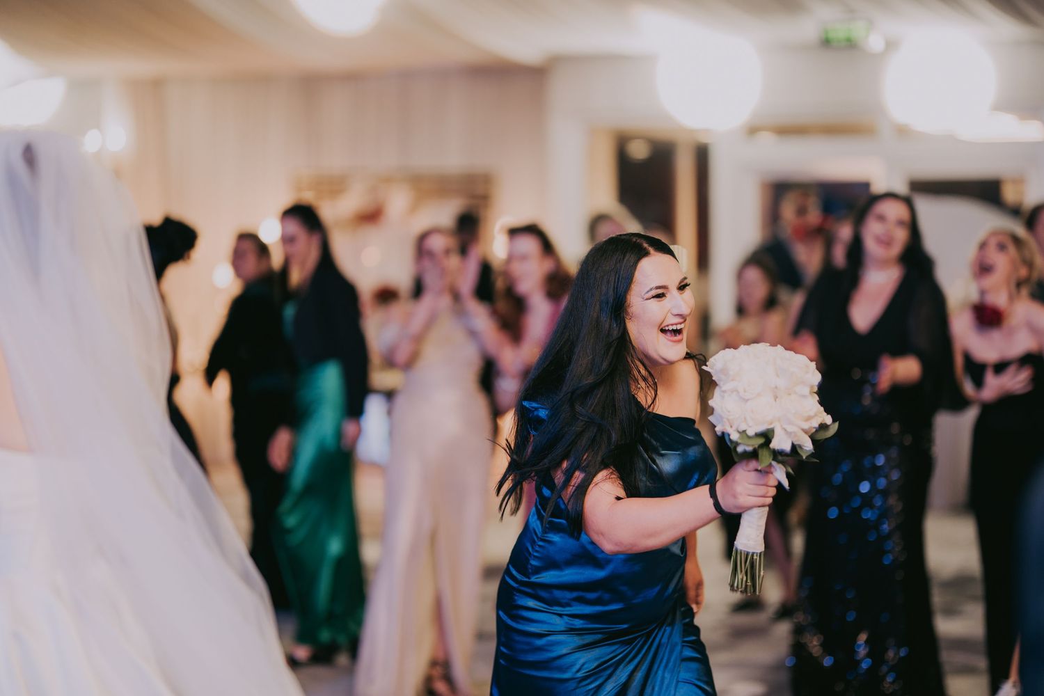 Excited bridesmaid in blue satin dress catches bridal bouquet of white roses at a wedding reception. Epicu Fotograf Drobeta-Turnu Severin