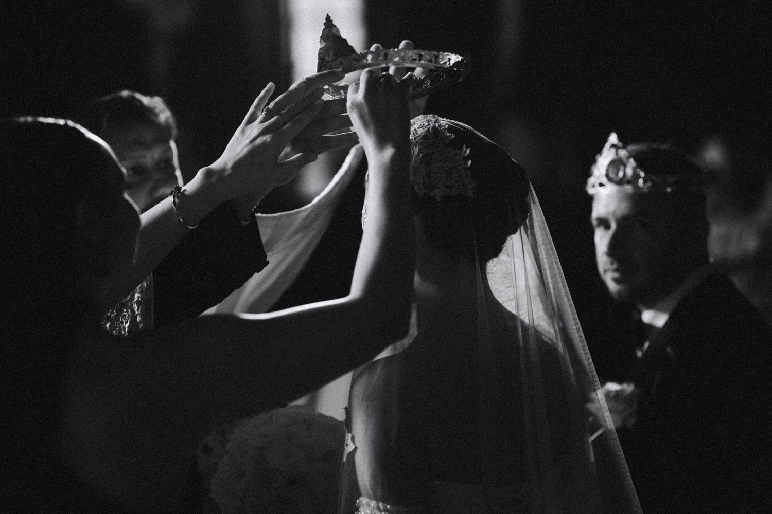Black and white photo of crowning ceremony during Orthodox wedding with ornate stefana crowns being placed.