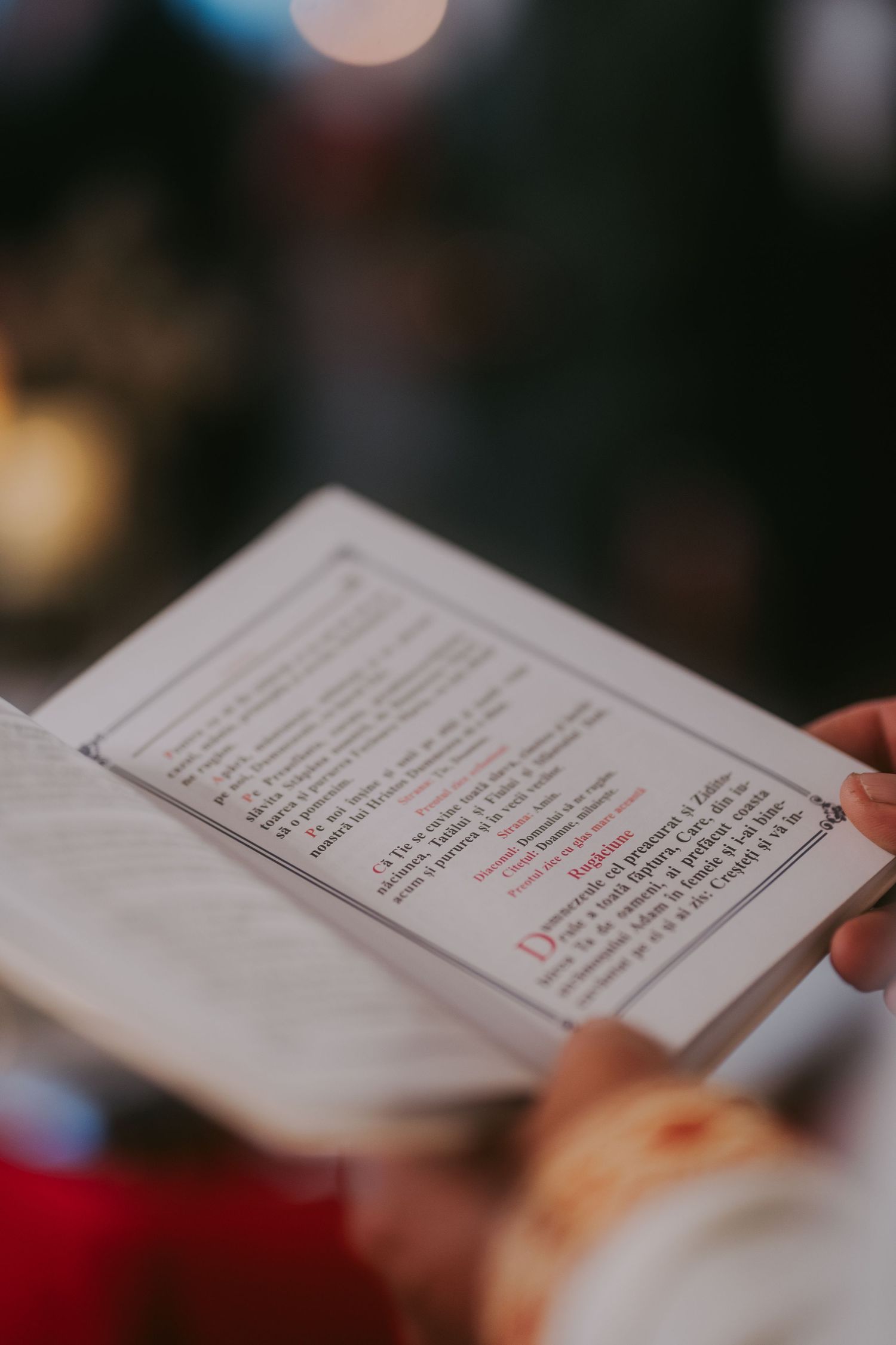 Close-up of religious ceremony booklet with red and black text held during Orthodox wedding service. Epicu Fotograf Drobeta-Turnu Severin