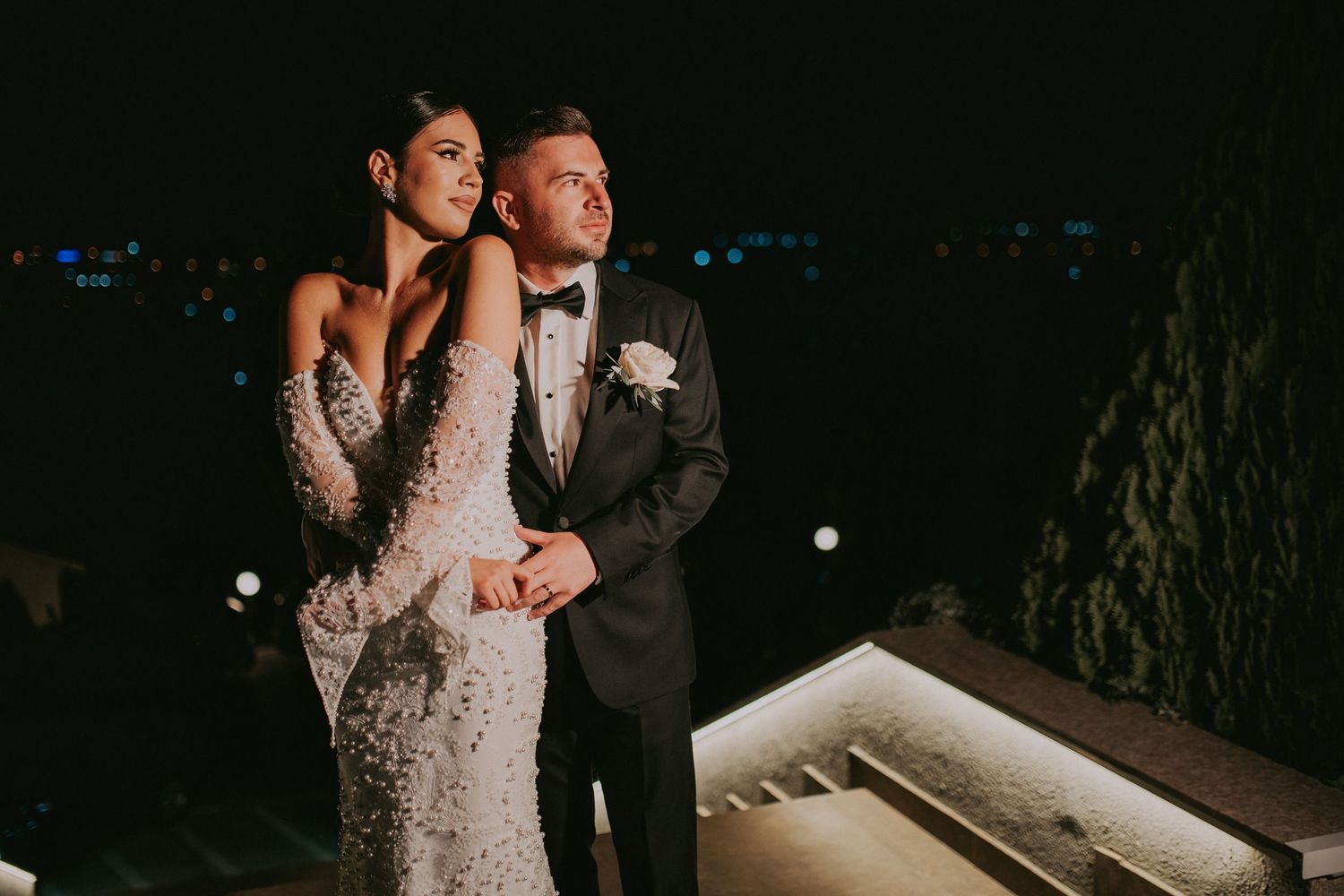 Elegant bride and groom pose together on a terrace under the night sky at their wedding reception.