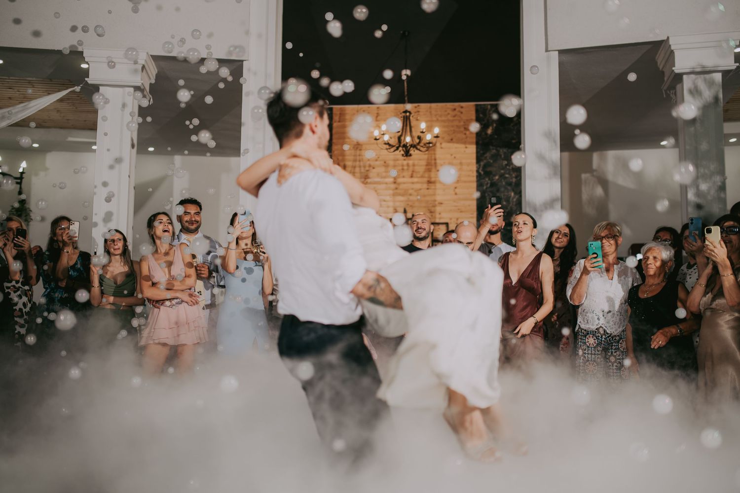 Groom lifting bride during first dance surrounded by bubbles and fog at reception.