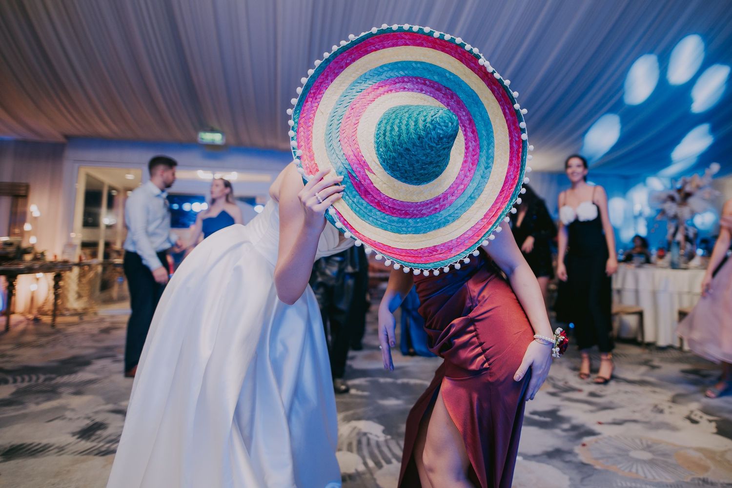 Two people playfully hiding behind a large colorful sombrero hat on a wedding dance floor. Epicu Fotograf Drobeta-Turnu Severin