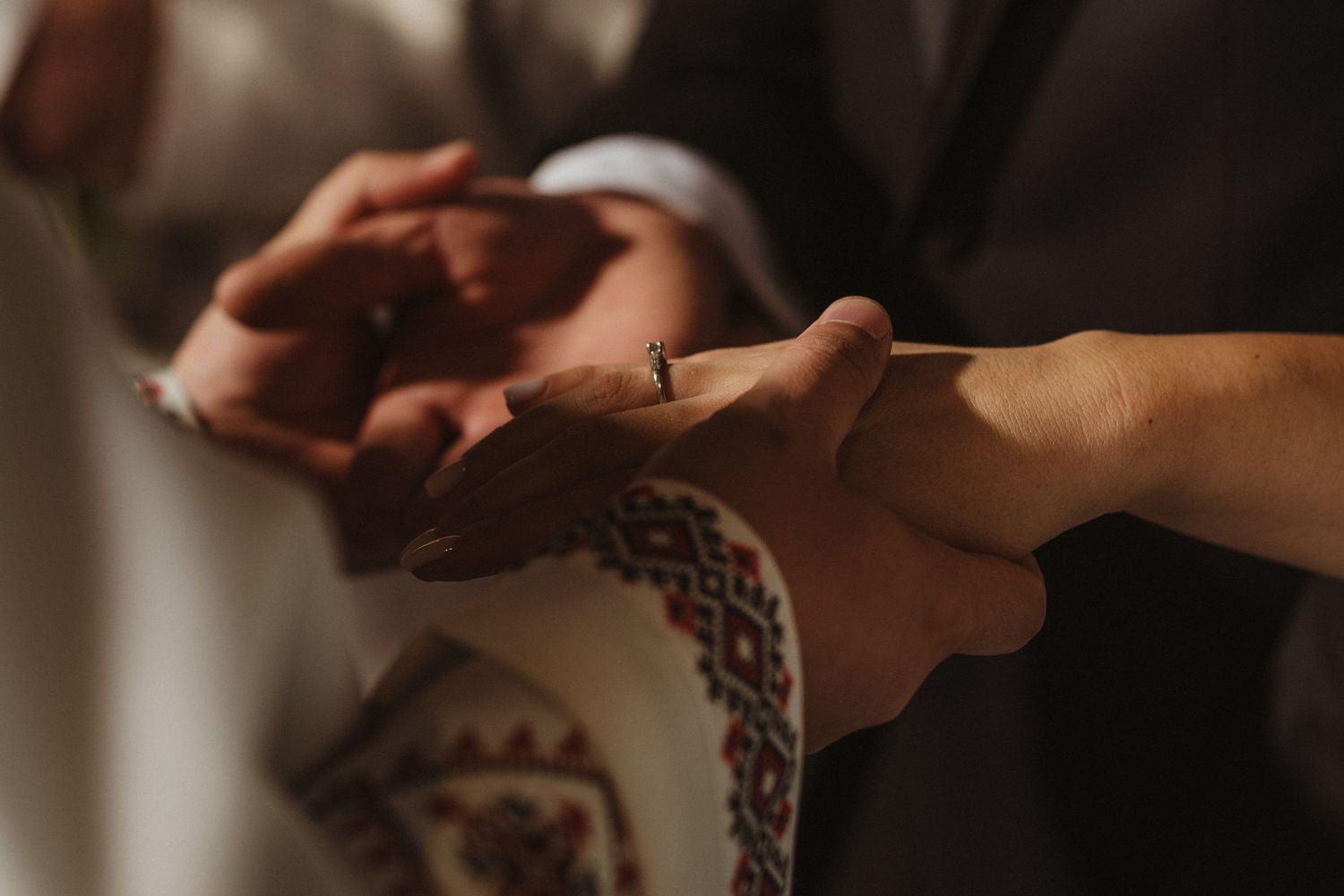 Priest places wedding ring on bride's hand during Orthodox marriage ceremony with embroidered vestment visible.