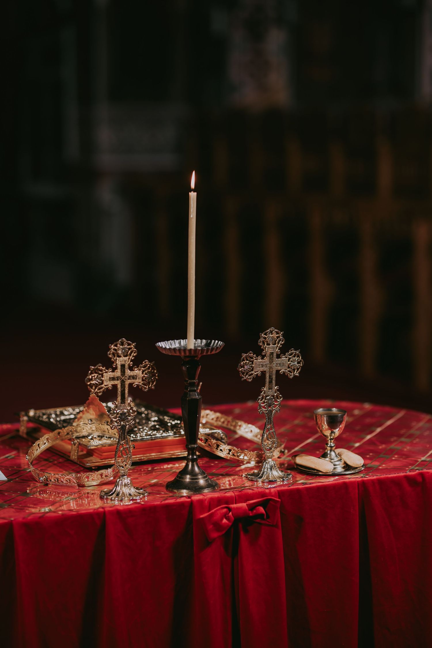 Orthodox wedding altar table with ornate crosses, lit candle, and red velvet cloth.