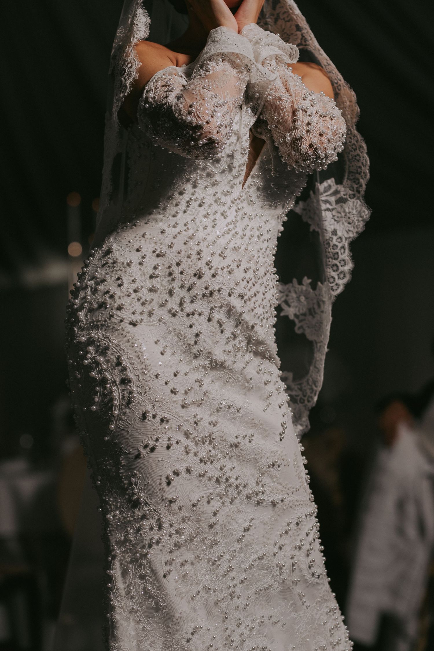 Close-up detail of a stunning pearl-beaded white wedding dress with lace gloves worn by a bride.