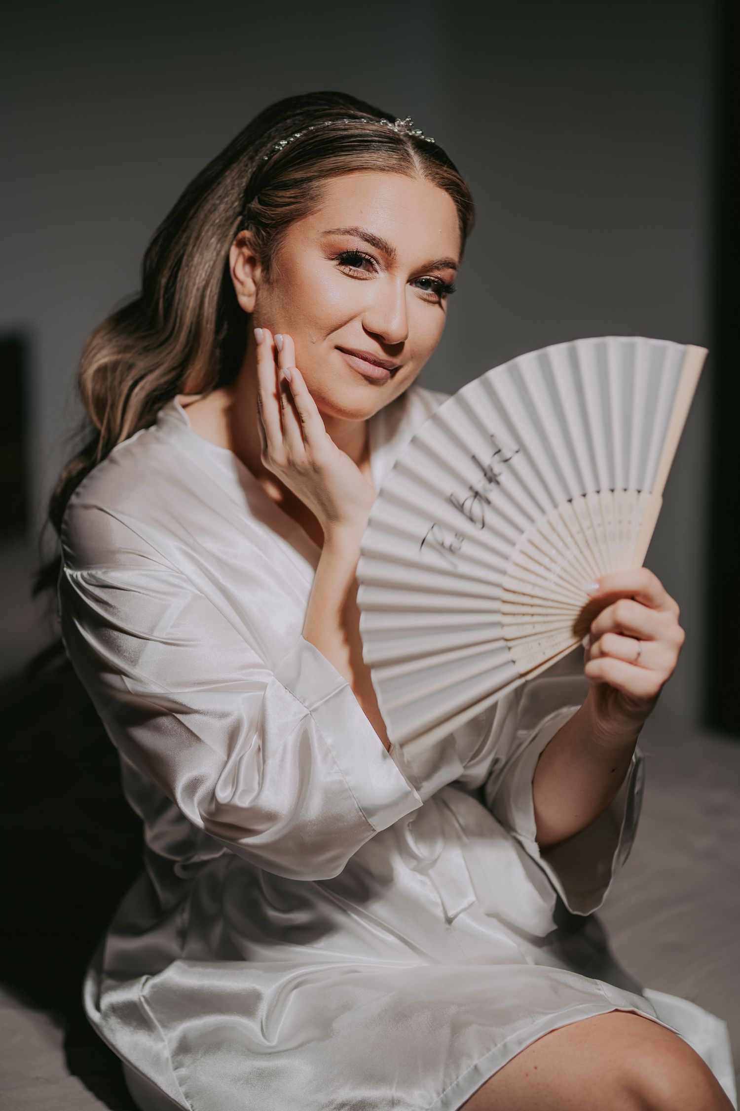 Bride in white satin robe holding a decorative hand fan while wearing a tiara headpiece. Epicu Fotograf Drobeta-Turnu Severin
