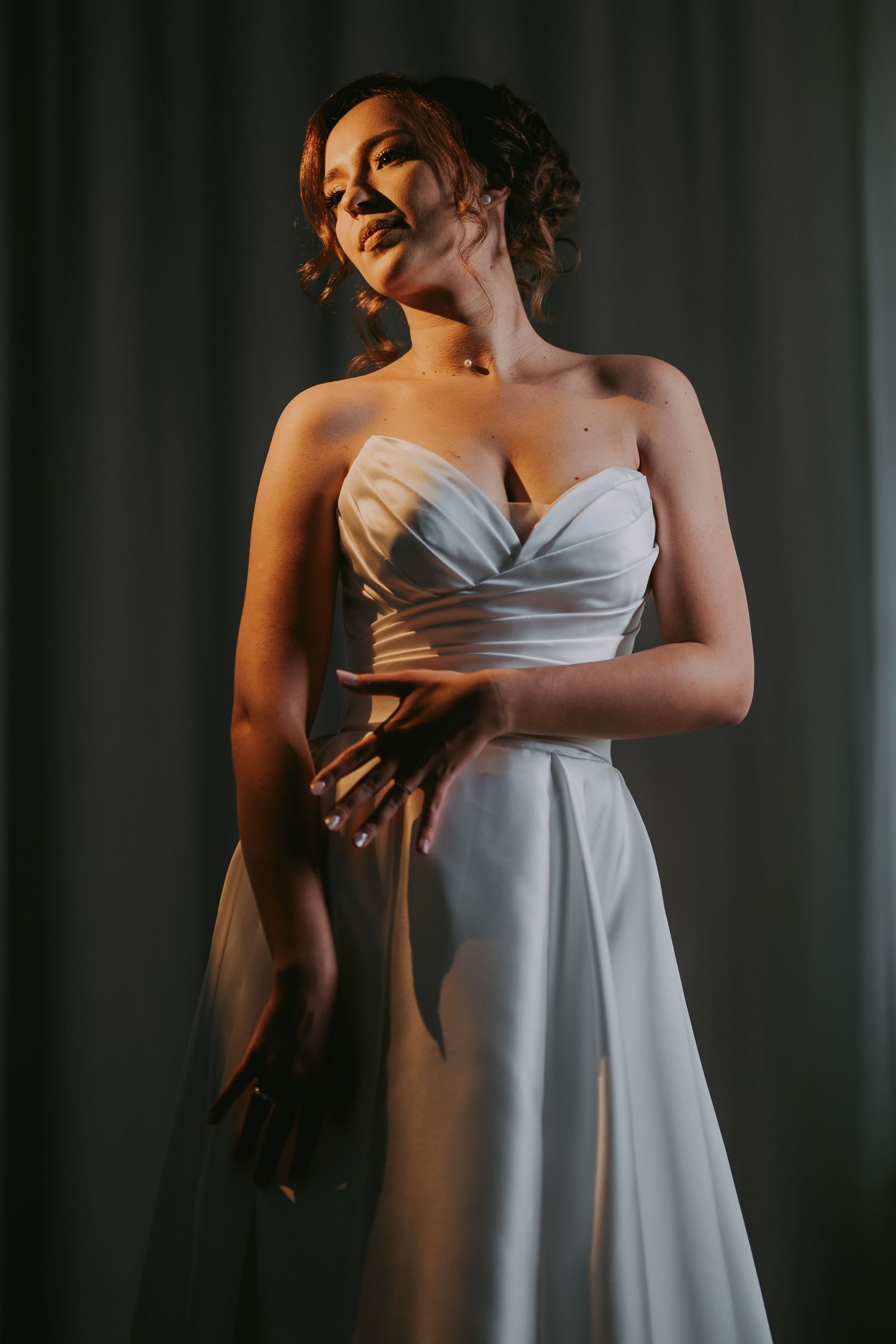 Elegant bride in a strapless satin ball gown posing dramatically in moody directional lighting. Epicu Fotograf Drobeta-Turnu Severin