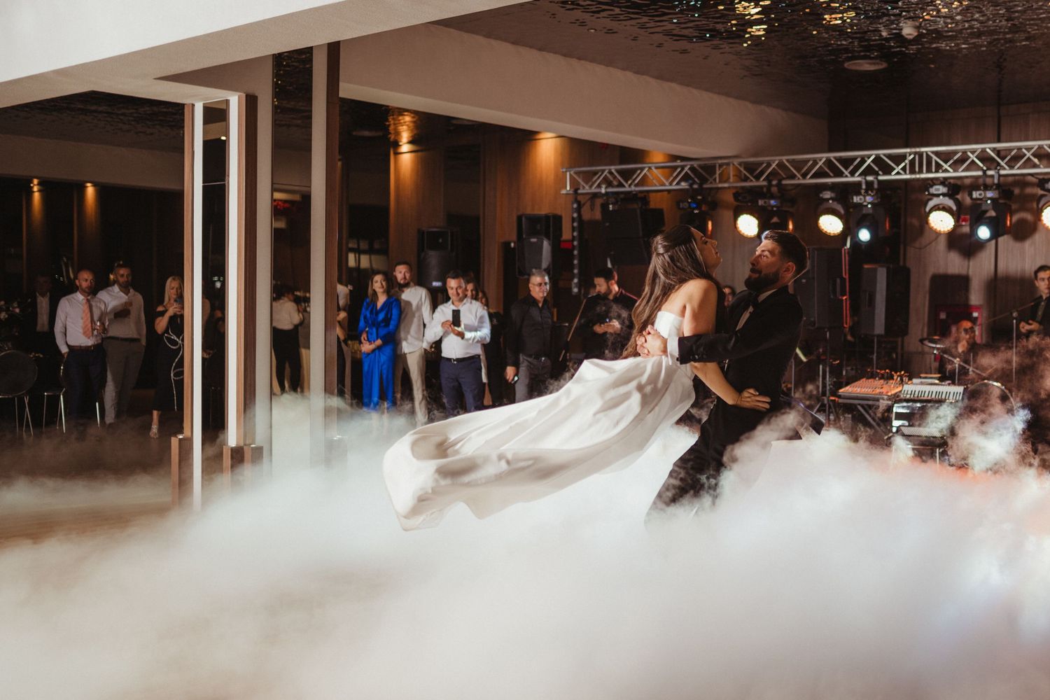 Bride and groom share first dance surrounded by dramatic fog machine effects at elegant wedding reception.