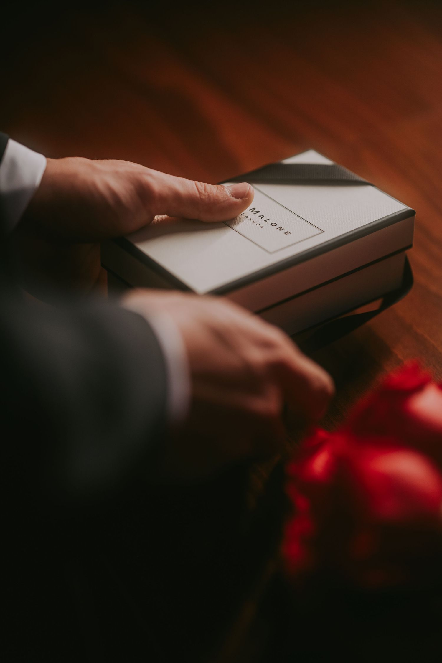 Groom opening a Jo Malone gift box with red roses on a wooden table.Epicu Fotograf Drobeta-Turnu Severin